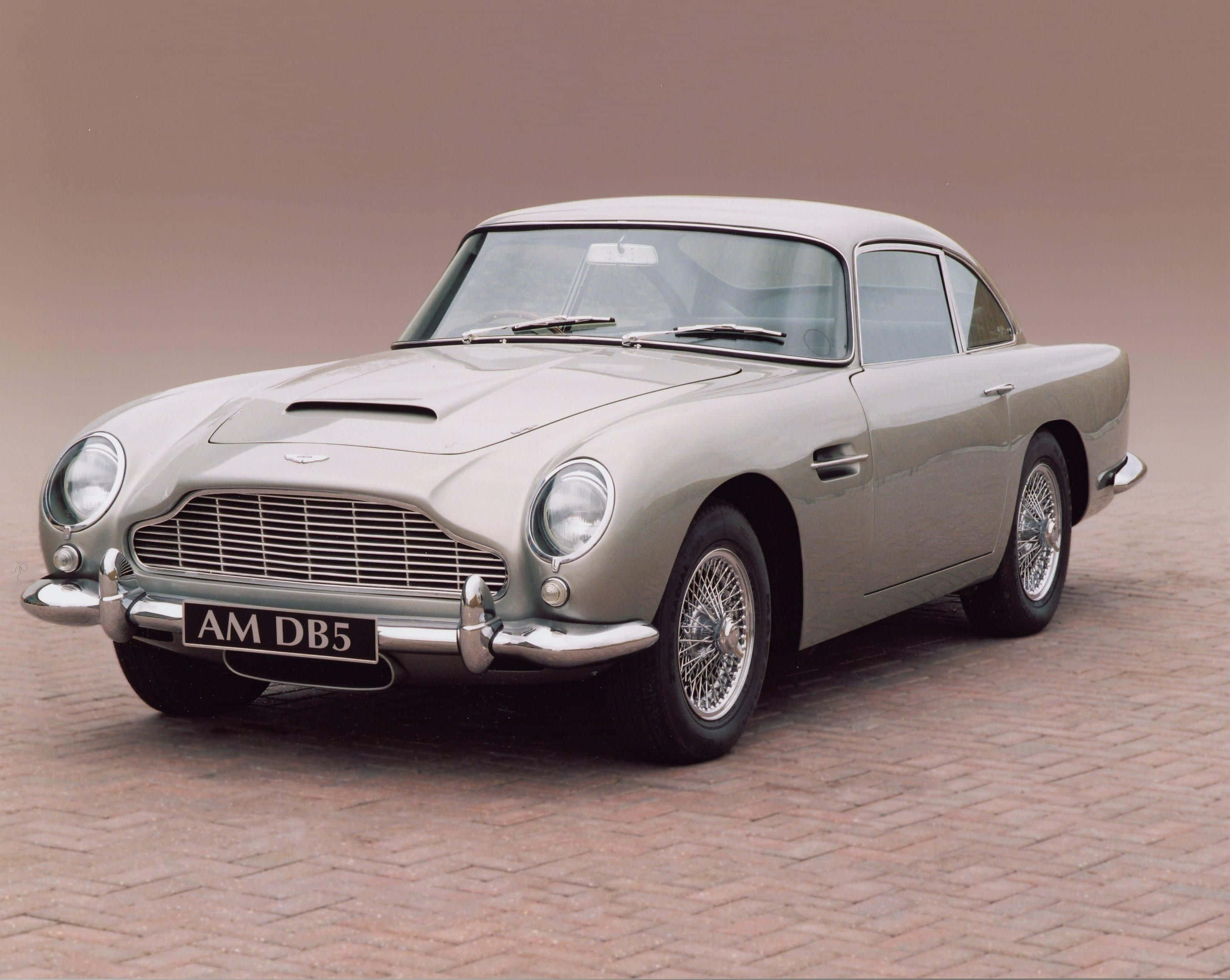 Aston Martin Db5 桌布 壁紙 — 一架時尚的銀色Aston Martin DB5經典汽車停泊在磚砌路面上，柔和的工作室燈光下。