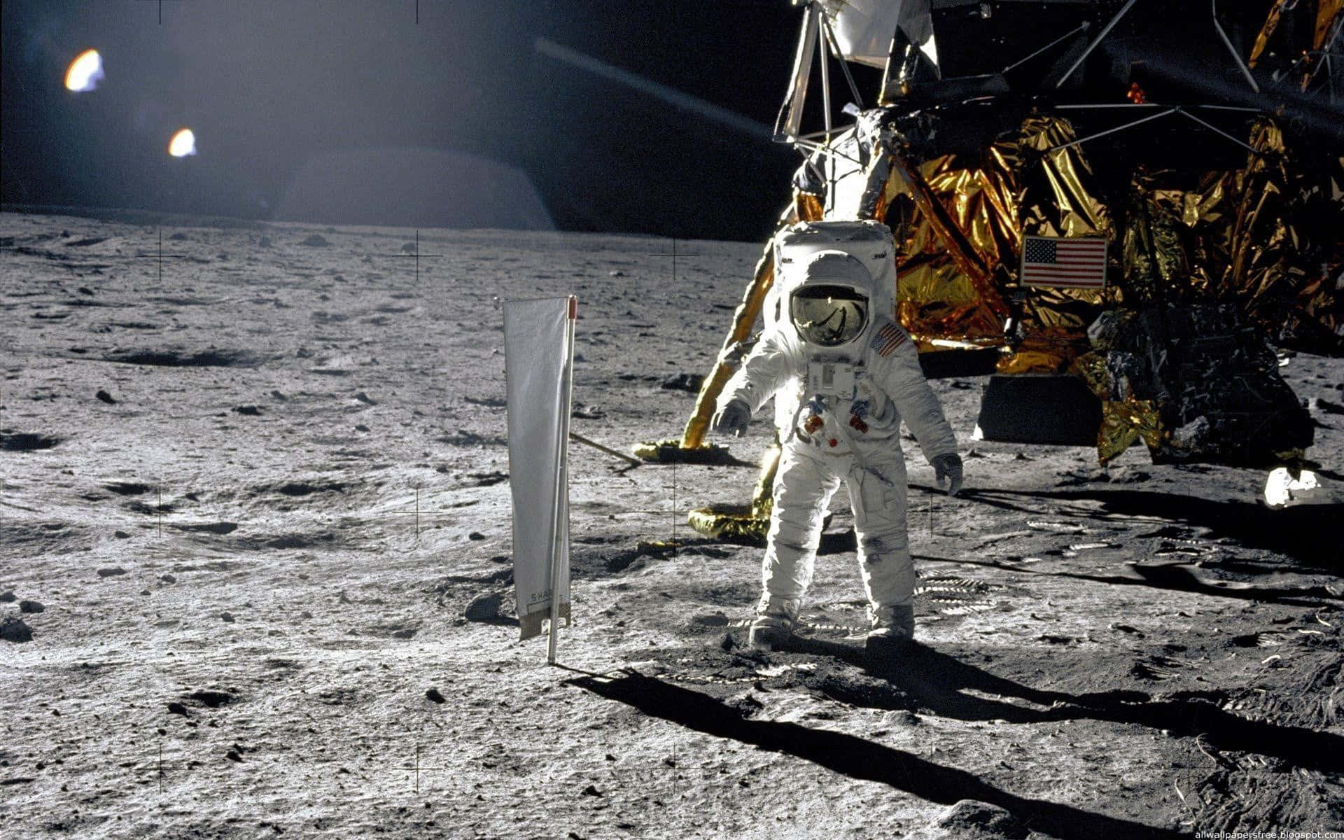 Neil Armstrong 桌布 壁紙 — 一名身穿白色太空衣的太空人站在月球灰色的表面上，旁邊有一個覆蓋金箔的登月艙和一面美國國旗。