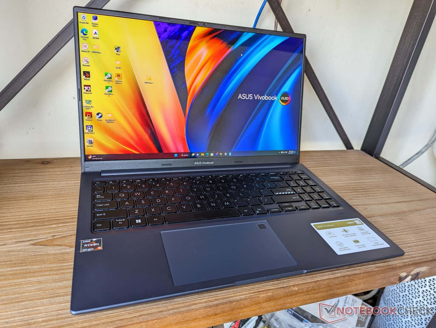 Asus OLED筆電畫面 壁紙 — 一部時尚的黑色ASUS Vivobook OLED手提電腦打開放在木桌上，顯示充滿活力的抽象桌布。
