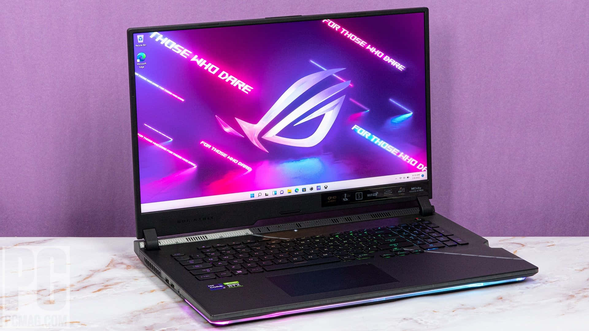 以 ASUS ROG 保持領先地位 壁紙 — 一部黑色電競手提電腦帶有發光RGB裝飾，打開放在大理石表面上，對著紫色牆壁顯示充滿活力的霓虹牆紙。