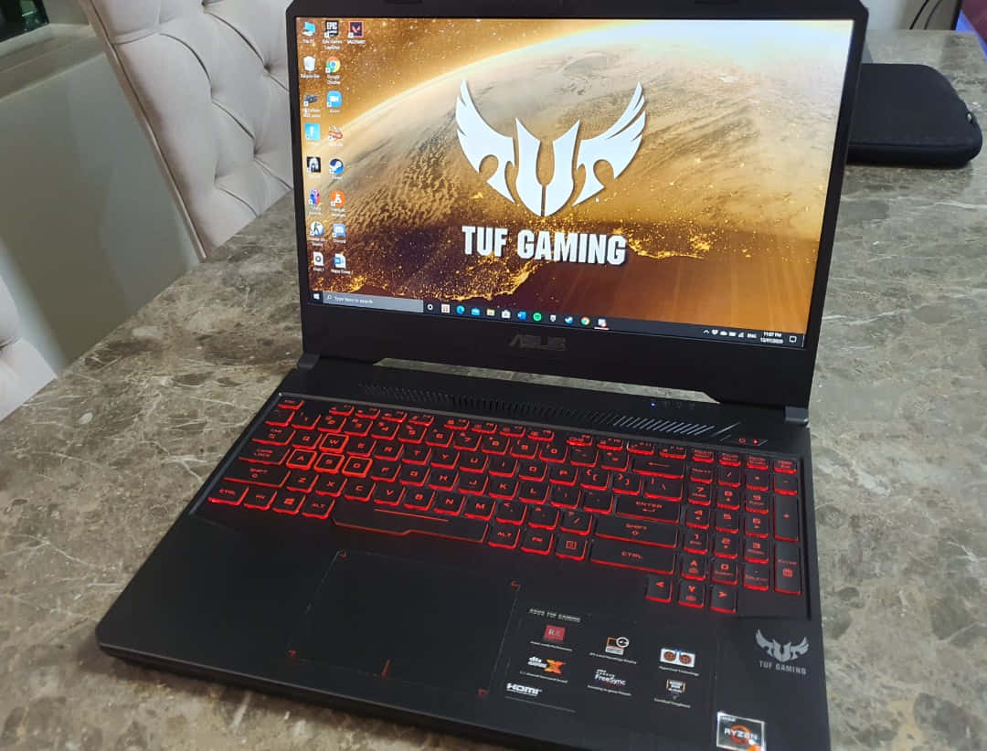 奢華 ASUS 筆電 壁紙 — 黑色ASUS TUF Gaming手提電腦，配備紅色發光背光鍵盤，打開放在大理石枱面上，顯示熾熱星球壁紙。
