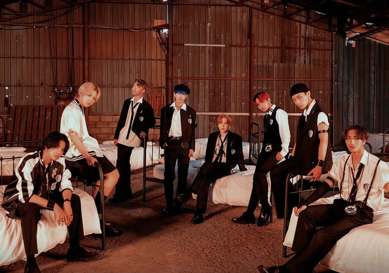 Ateez：隨時隨地搖滾你的桌面！ 壁紙 — 七位時尚年輕男士身穿黑白搭配服裝，在溫暖燈光的質樸倉庫中自信地躺在床上擺姿勢。