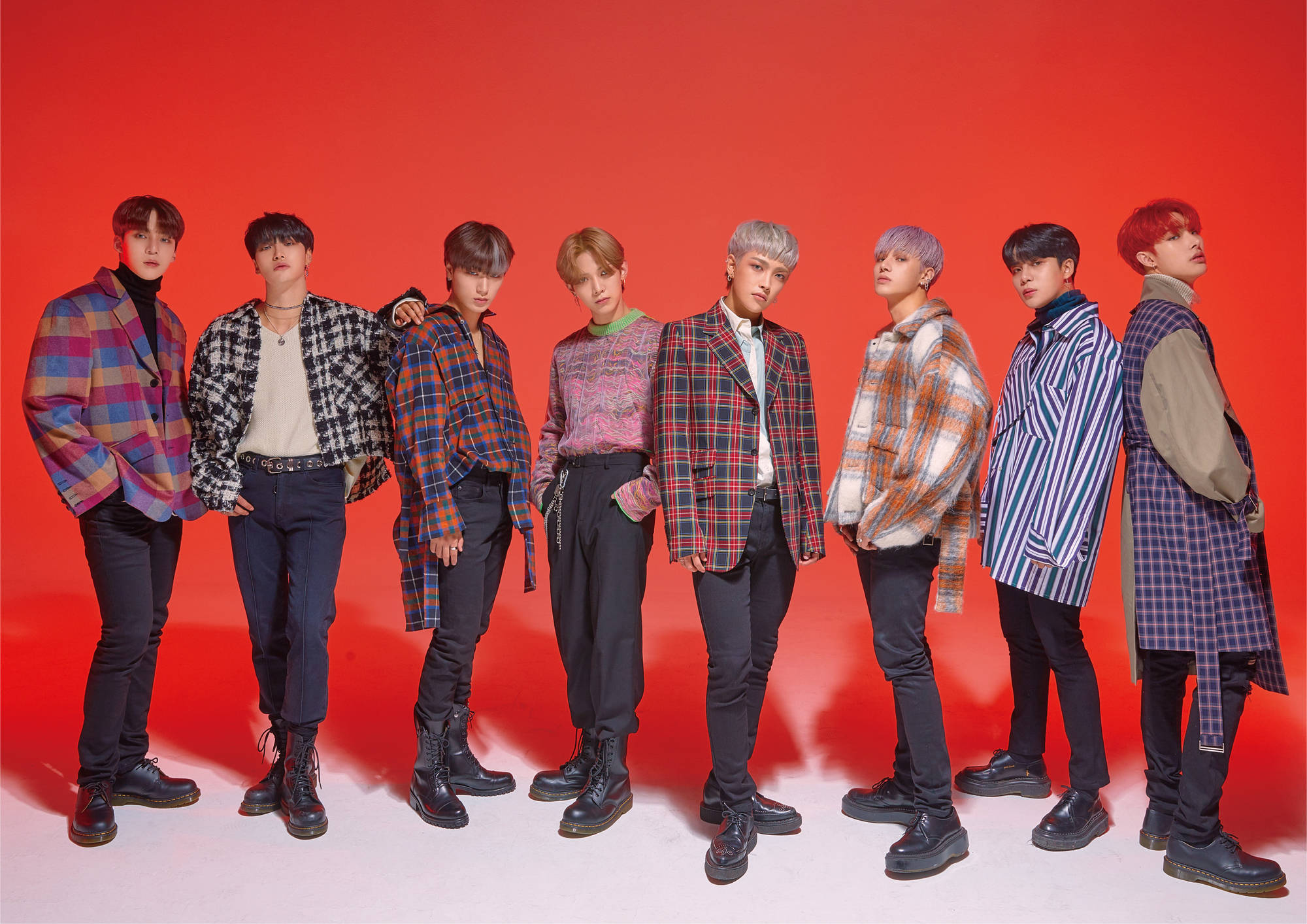 ATEEZ 紅色背景 壁紙 — 七位時尚年輕男子身穿彩色格紋外套和靴子，在鮮紅色的攝影棚背景前自信擺姿勢。
