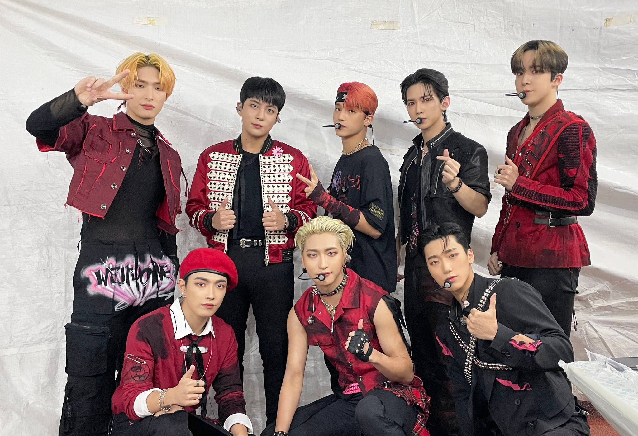 七位K-pop偶像穿著紅色和黑色服裝拍照。