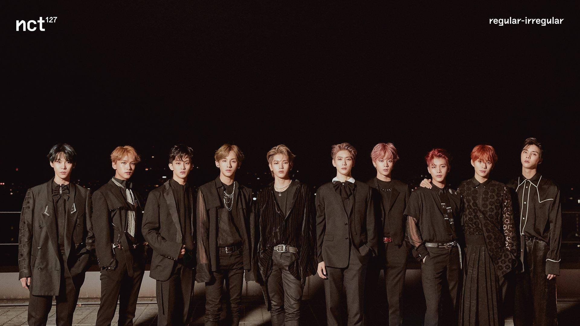 ATEEZ 黑色美學桌面 壁紙 — 九位時尚年輕男士身穿深色西裝，在夜間城市天際線背景下自信地擺姿勢。