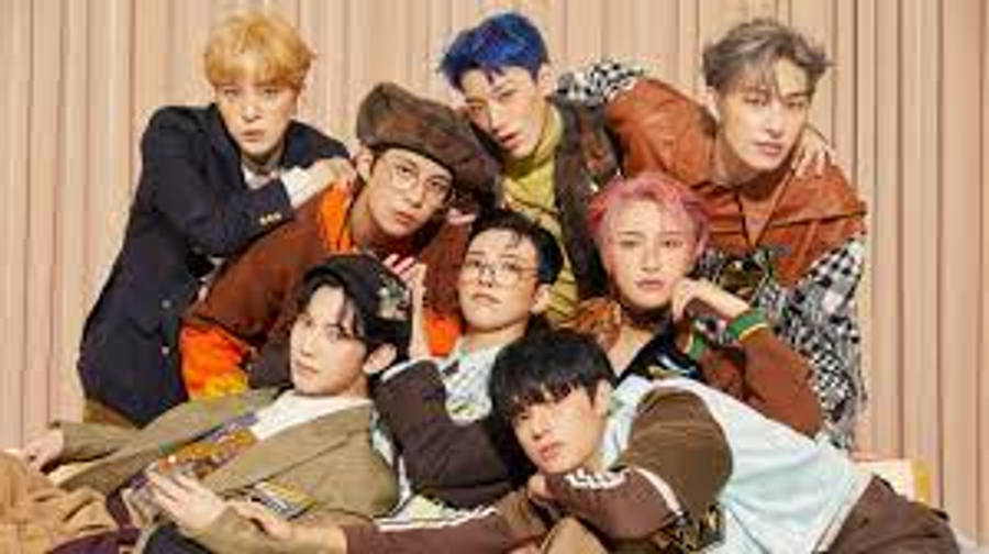 ATEEZ擁抱互動桌面壁紙 壁紙 — 七位時尚年輕男士穿著色彩繽紛的服裝，在暖色調條紋背景前隨意擺姿勢。