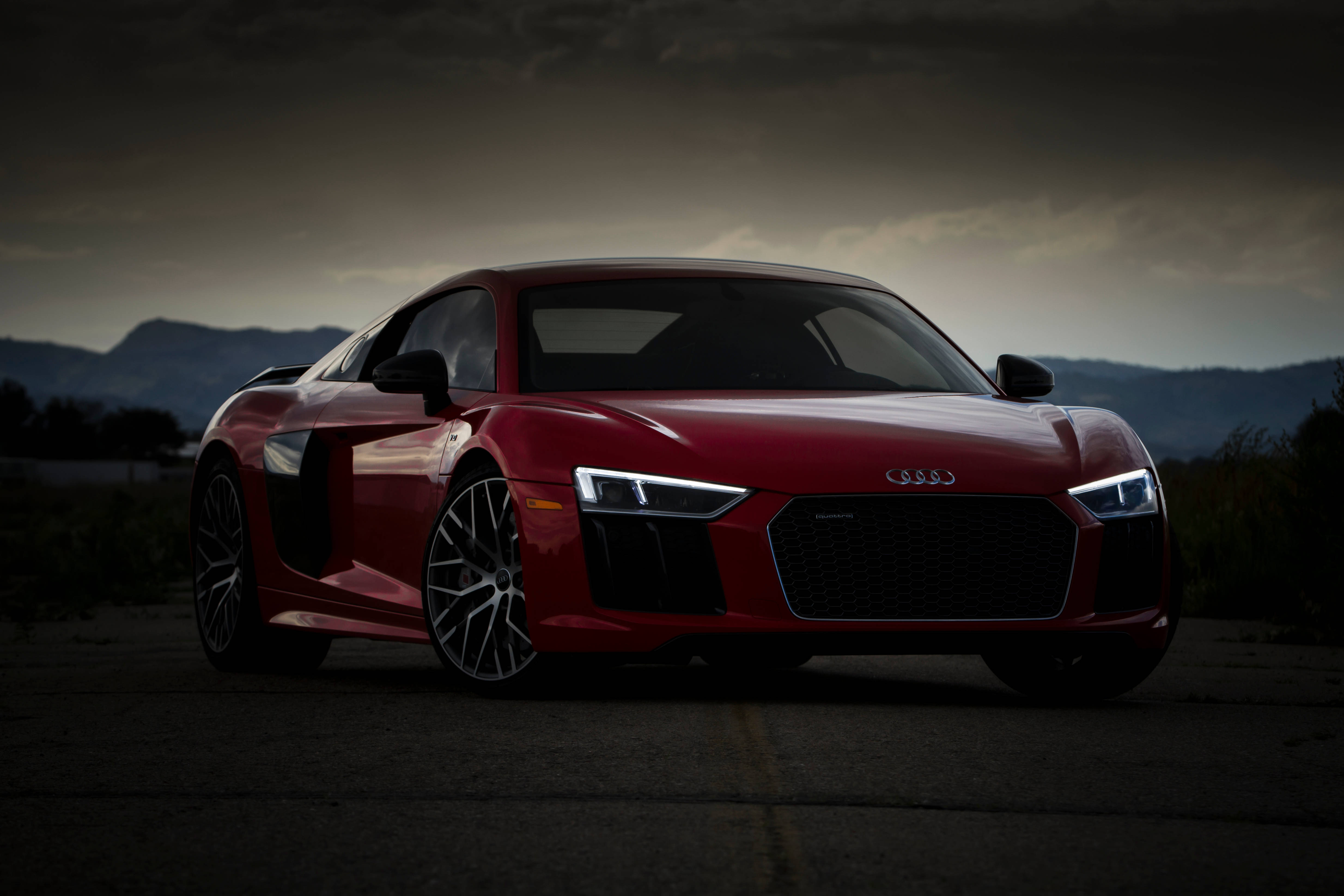 紅色 Audi R8 運動跑車 壁紙 — 一架流線型紅色奧迪R8跑車停泊在黑暗的道路上，背景有山脈，天空風暴密佈。