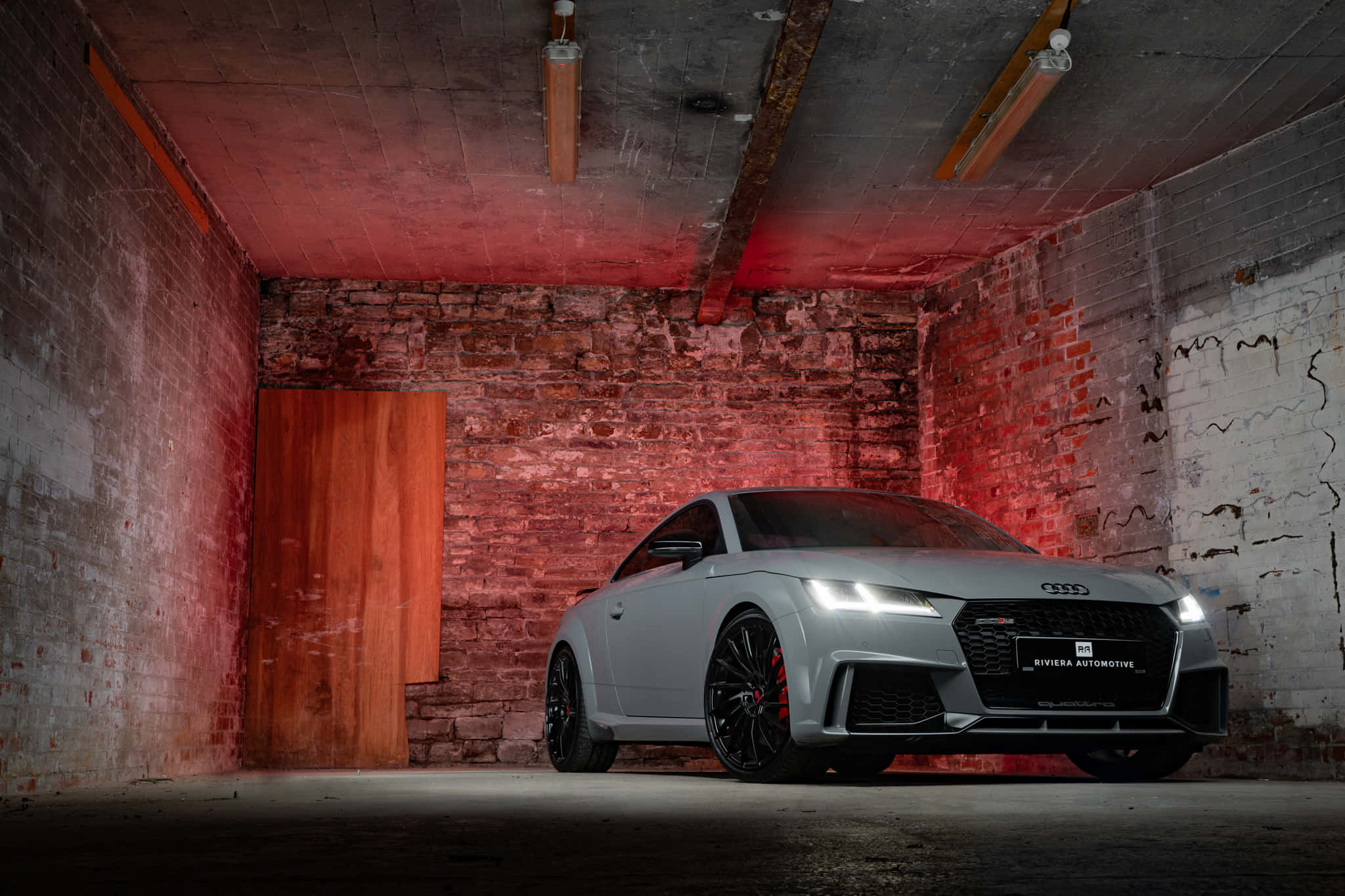 Audi Tt Rs 桌布 壁紙 — 一輛時尚的銀色奧迪 TT RS 轎跑車在磚牆鄉村風格車庫內，在戲劇性的紅色燈光下閃閃發光。