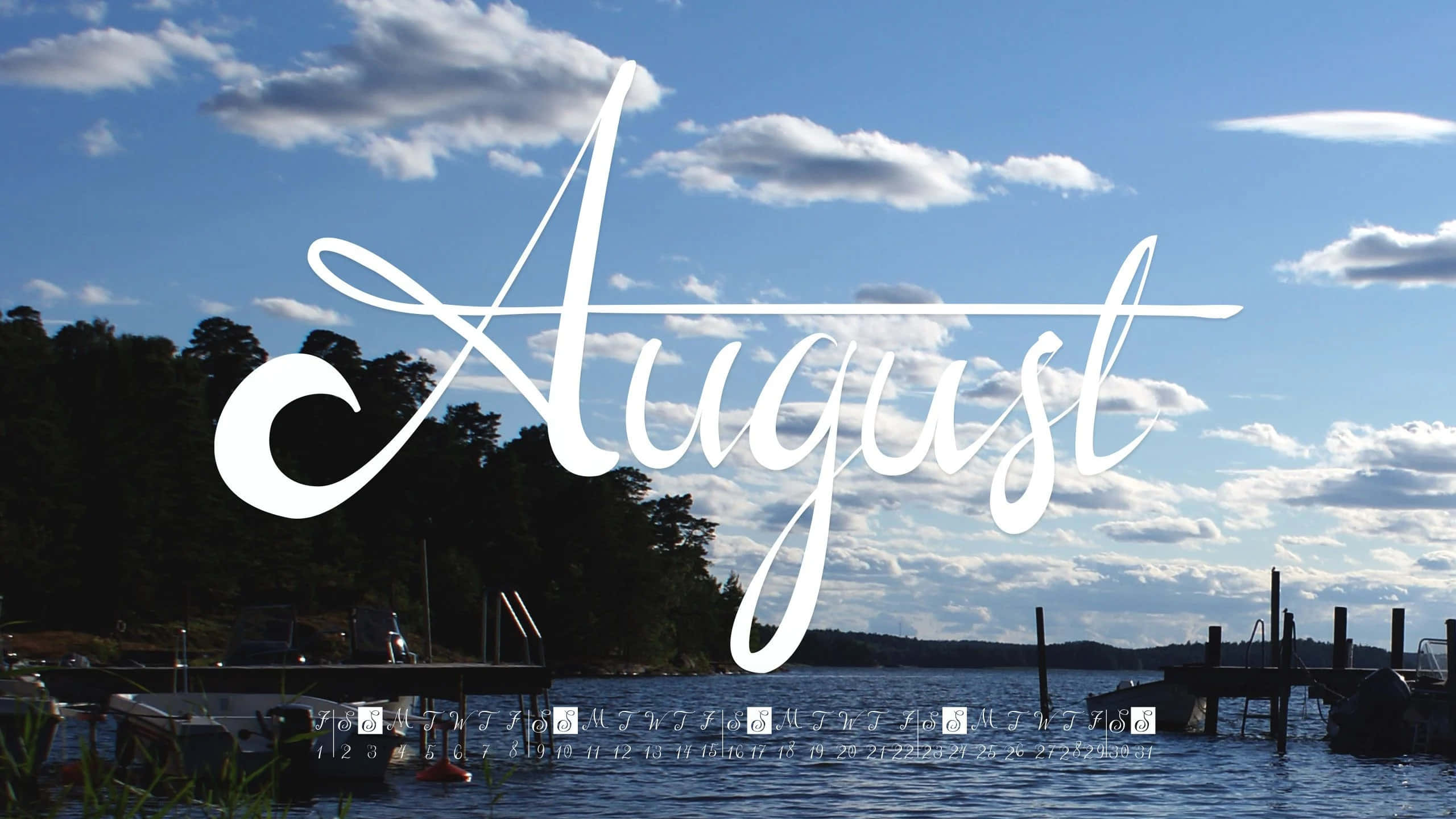 August 桌布 壁紙 — 「August」這個詞以優雅的白色字體漂浮在寧靜的湖面上，湖上有碼頭、船隻和樹木成蔭的湖岸，上方是明亮的藍天和蓬鬆的白雲。