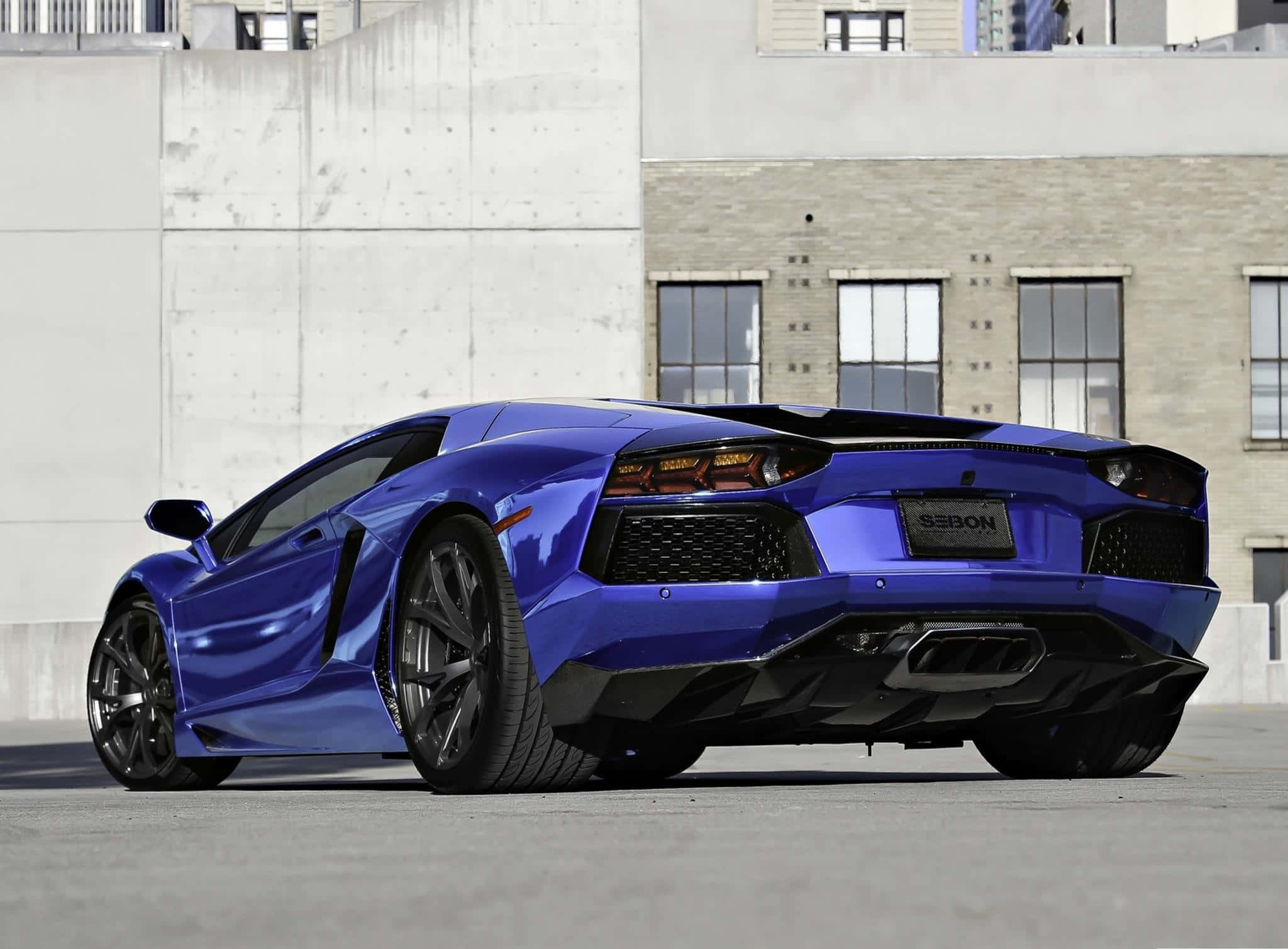 深藍色蘭博基尼Aventador流線型設計 壁紙 — 一架亮藍色林寶堅尼Aventador跑車停泊在混凝土上，背景是城市建築物。
