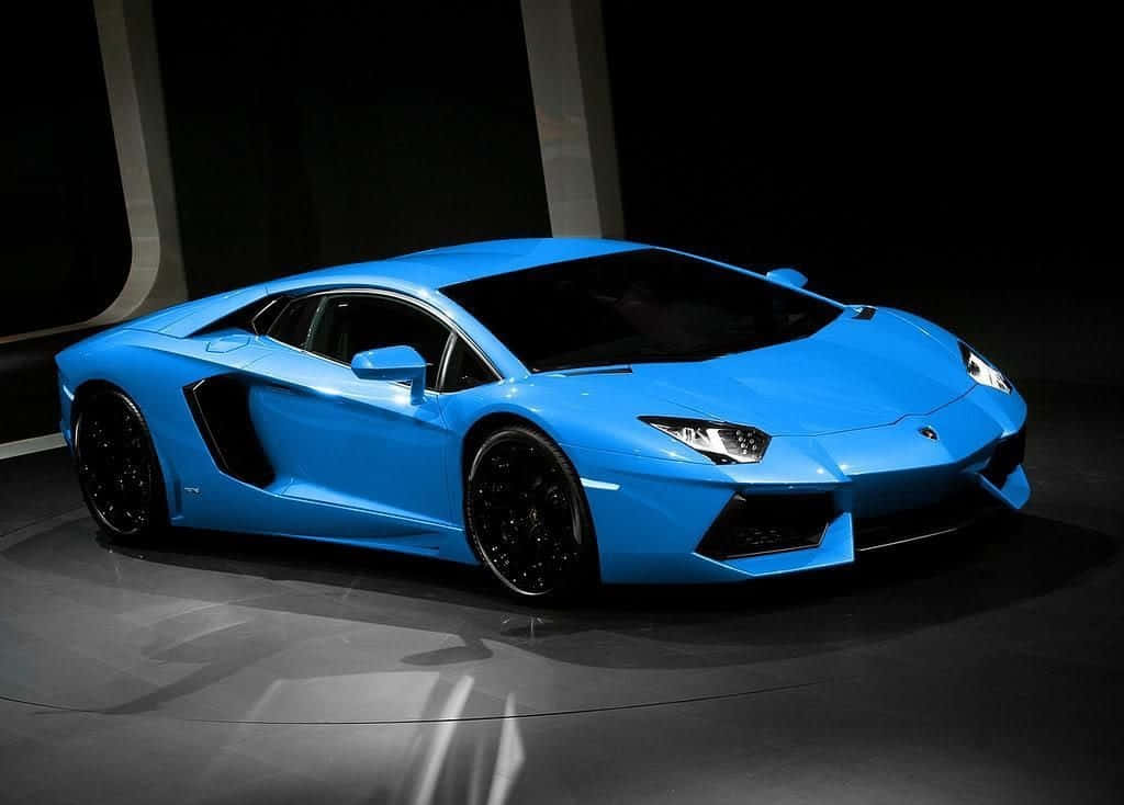 運動型藍色蘭博基尼Aventador跑車 壁紙 — 一輛充滿活力的藍色林寶堅尼Aventador跑車在黑暗反光舞台上的工作室燈光下閃閃發光。