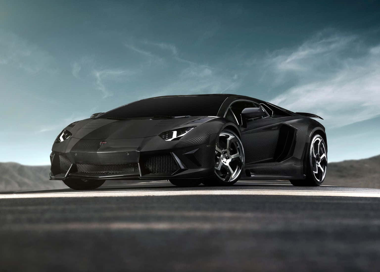 黑色鑽石車蘭博基尼Aventador 壁紙 — 一架時尚的黑色林寶堅尼Aventador跑車，帶有碳纖維細節，在陰沉天空下的沙漠道路上蓄勢待發。