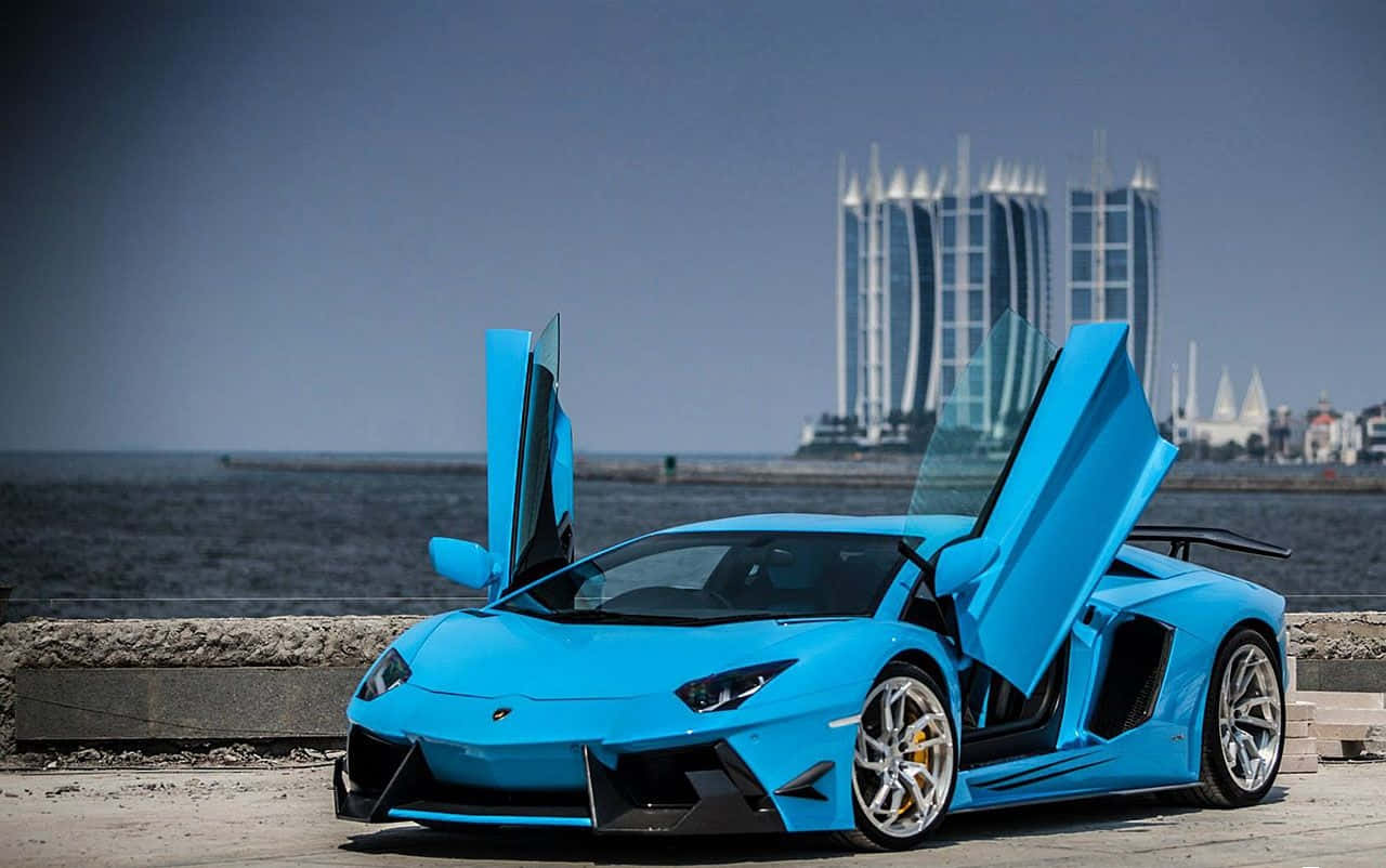 藍色蘭博基尼Aventador炫酷車門 壁紙 — 一架鮮藍色林寶堅尼Aventador打開鷗翼車門，停在海濱長廊上，背景是現代摩天大樓。
