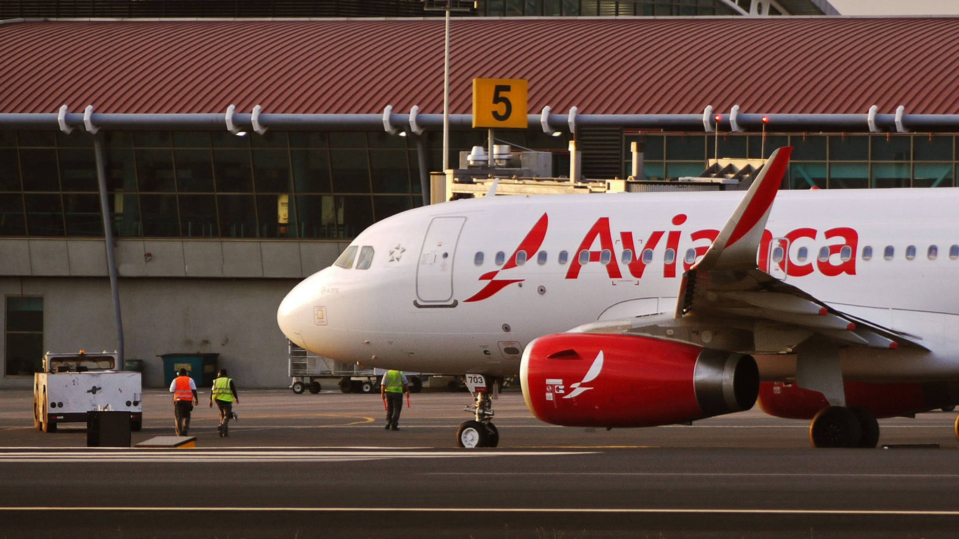 Avianca 飛機在機場閘口，地勤人員在日落時分於附近行走。
