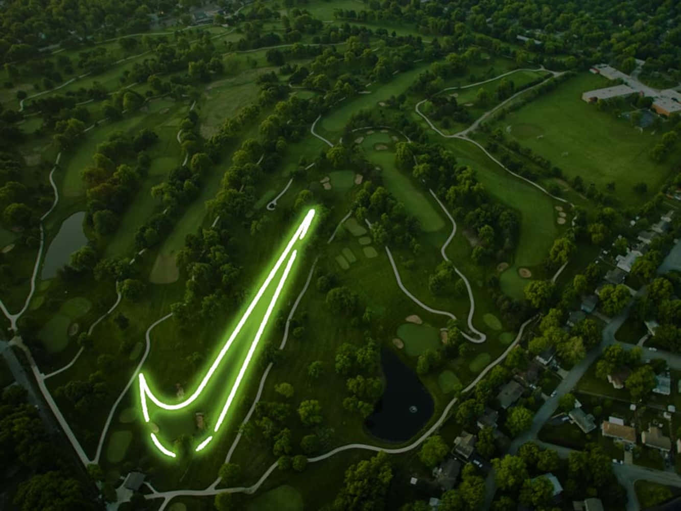 與朋友在Awesome Golf享受下一場高爾夫球賽吧！ 壁紙 — 黃昏時分，在高爾夫球場上雕刻出發光的綠色Nike勾號的鳥瞰圖。