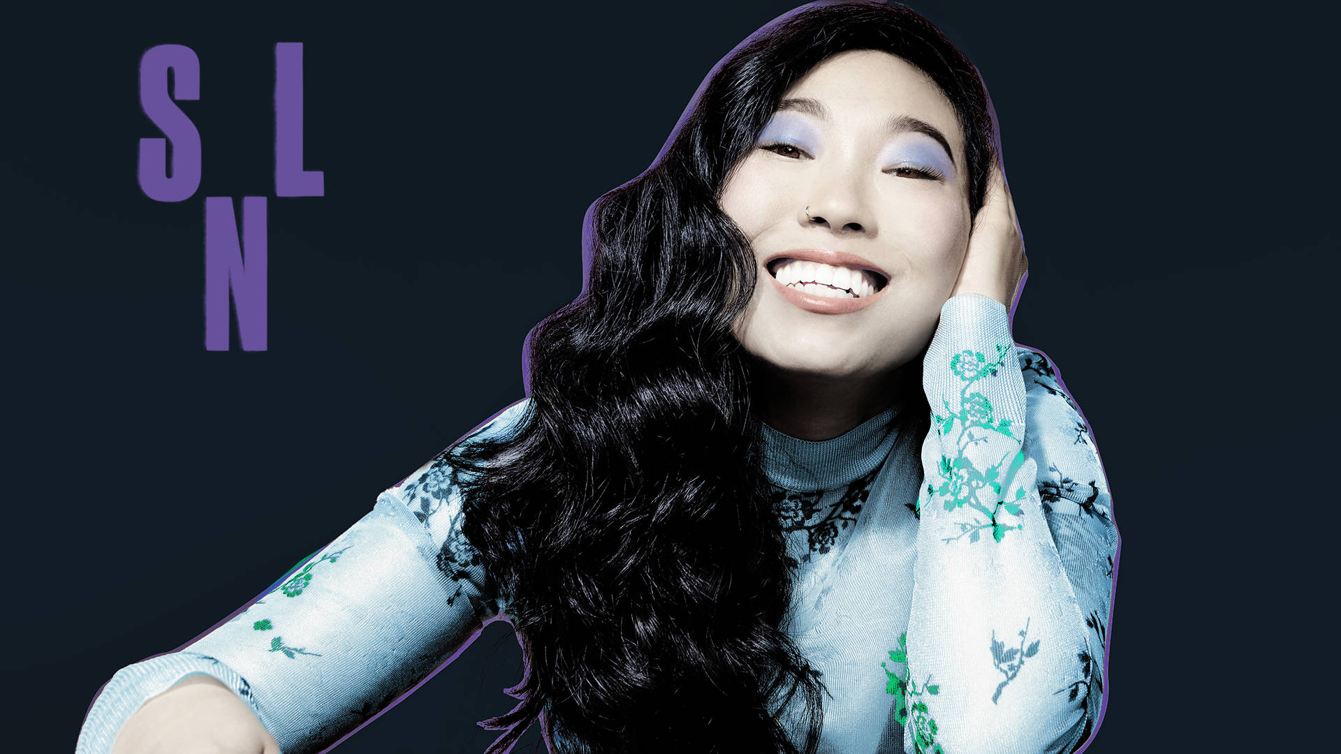 Awkwafina 背景有 SNL 字樣的照片 壁紙 — 一位長長深色頭髮、塗著紫色眼影的快樂女性，在深色背景襯托下，手托著頭微笑，背景有紫色字樣。