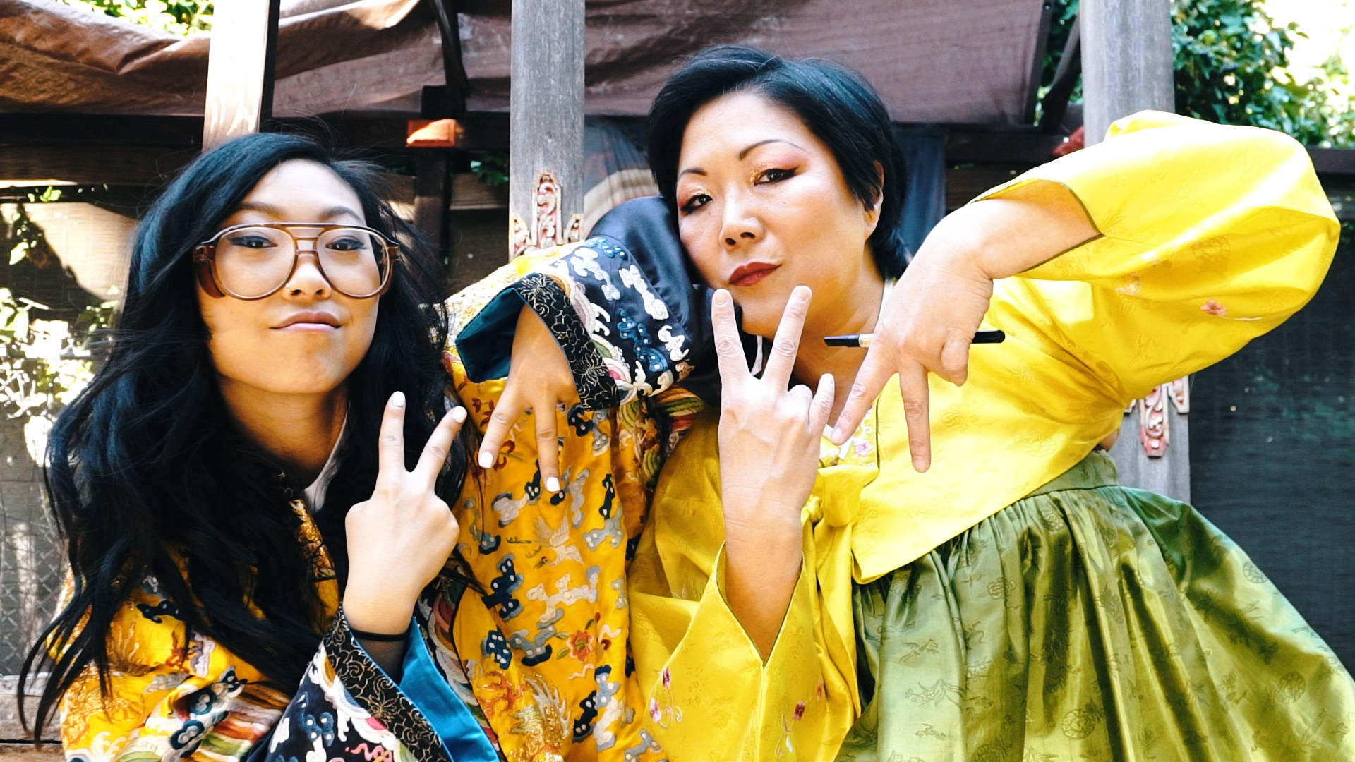Awkwafina 與Margaret韓服照 壁紙 — 兩位身穿鮮豔傳統長袍的女性在明亮的日光下，俏皮地擺出和平手勢。