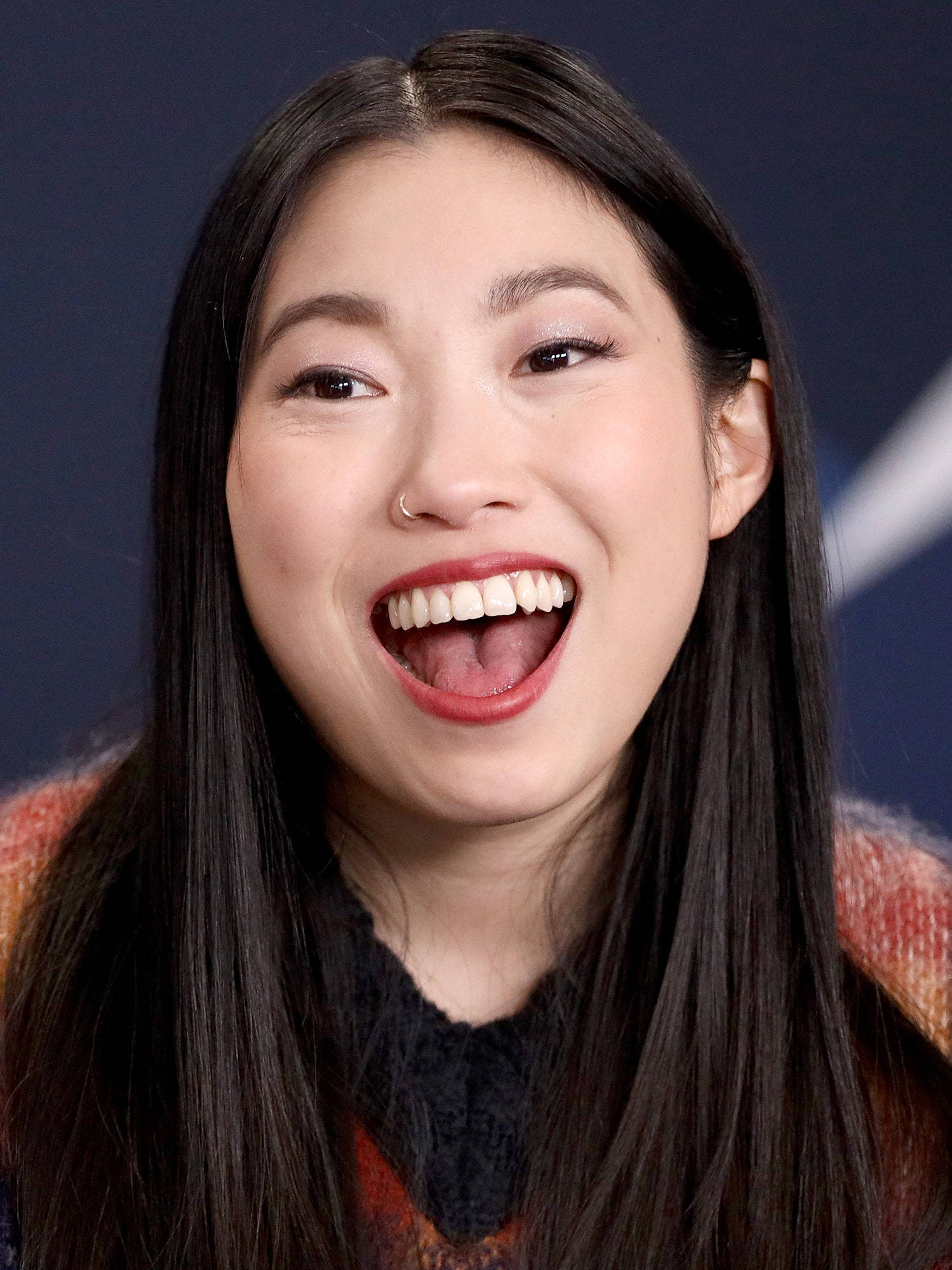 Awkwafina 近距離肖像照 壁紙 — 一位長黑髮的快樂女性在深藍色背景下張嘴大笑，露出潔白的牙齒。