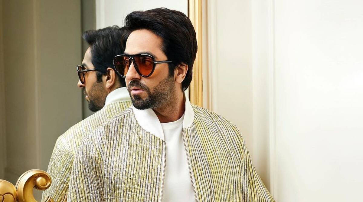 Ayushmann Khurrana 穿銀金夾克 壁紙 — 一位時尚男士身穿金色條紋外套和太陽眼鏡，站在豪華室內的鏡子前。
