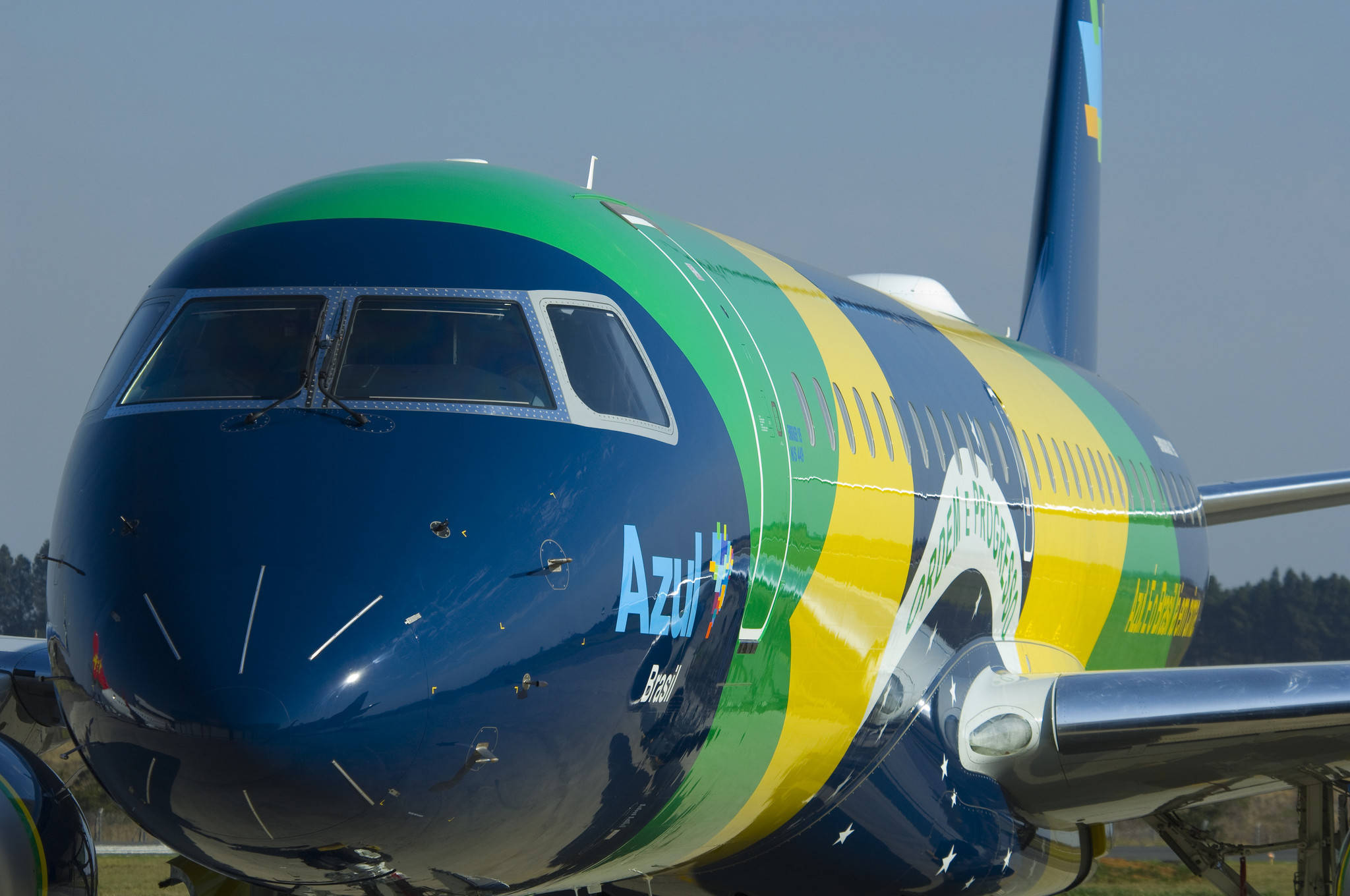 Azul航空藍色客機正面 壁紙 — 巴西藍色航空飛機的特寫，帶有鮮豔的綠色、黃色和藍色塗裝，停在晴朗天空下的停機坪上。