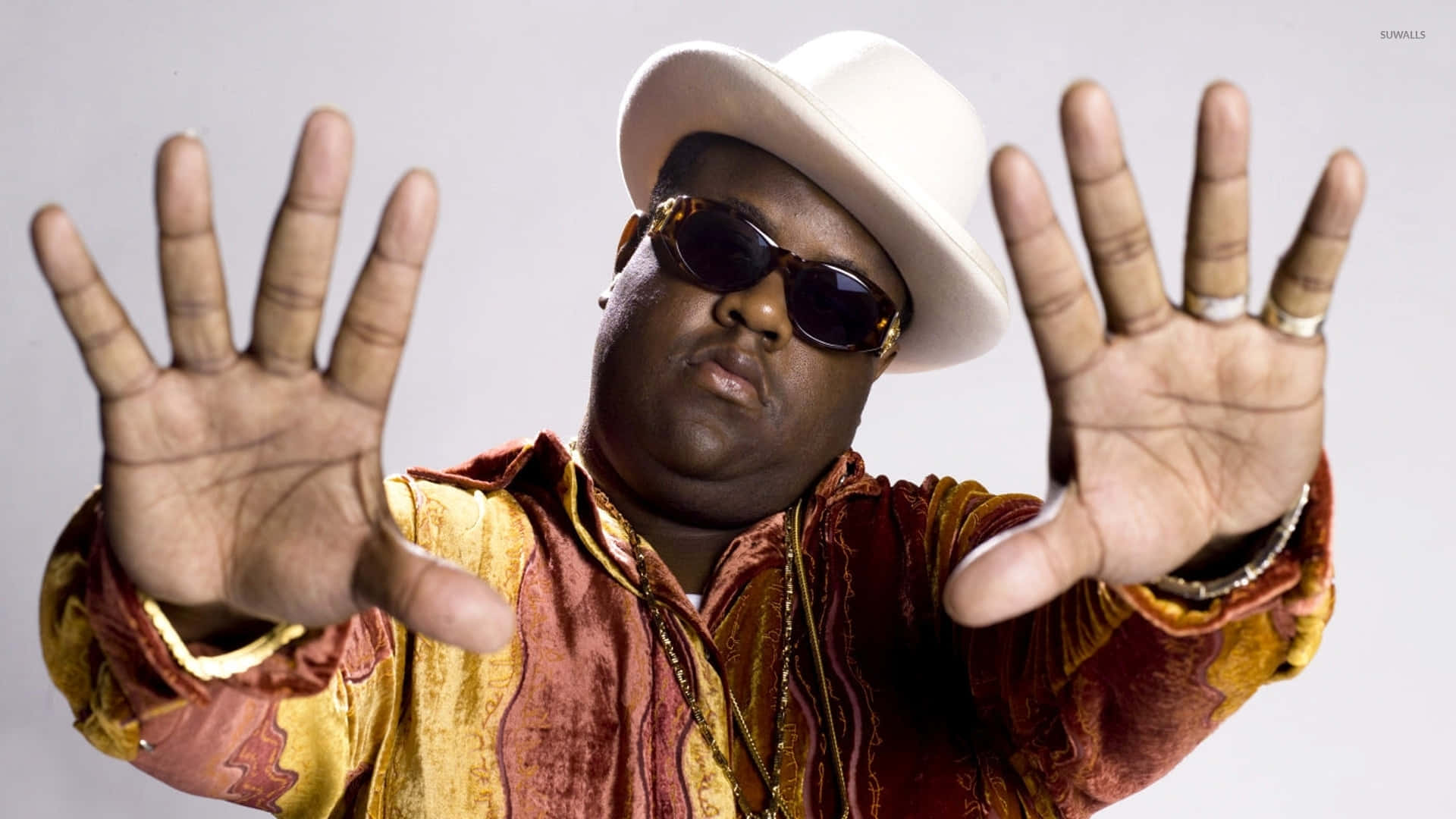 B.I.G. - 布魯克林最偉大的傳奇 壁紙 — 一個戴白色帽子和太陽眼鏡的男人，在純色背景前雙手向前伸出，手指張開。