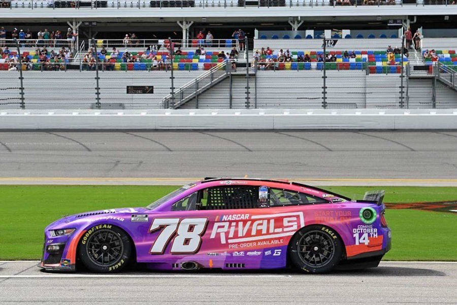 B.J. McLeod 在 NASCAR 賽事中激烈競速 壁紙 — 一輛充滿活力的紫色和粉紅色NASCAR賽車（78號）在賽道上飛馳，背景是色彩繽紛的看台。