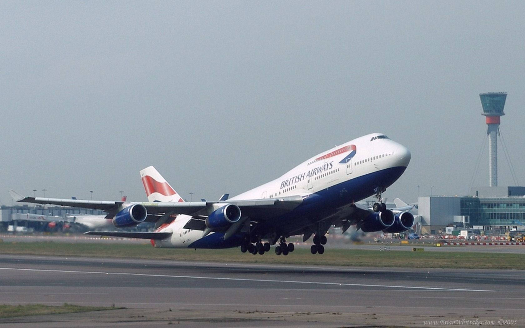 英國航空波音 B747-400 起飛 壁紙 — 一架英國航空波音747在陰天背景下從跑道起飛，背景有機場建築物和管制塔。