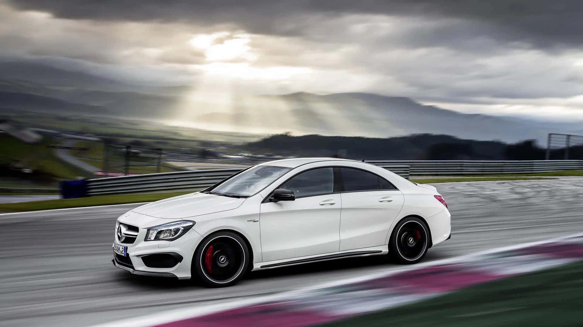 Mercedes Benz Cla-class 桌布 壁紙 — 一輛白色 Mercedes-AMG CLA45 S 在賽道上奔馳，戲劇性的陽光穿透暴風雲層，照耀在起伏的山丘上。