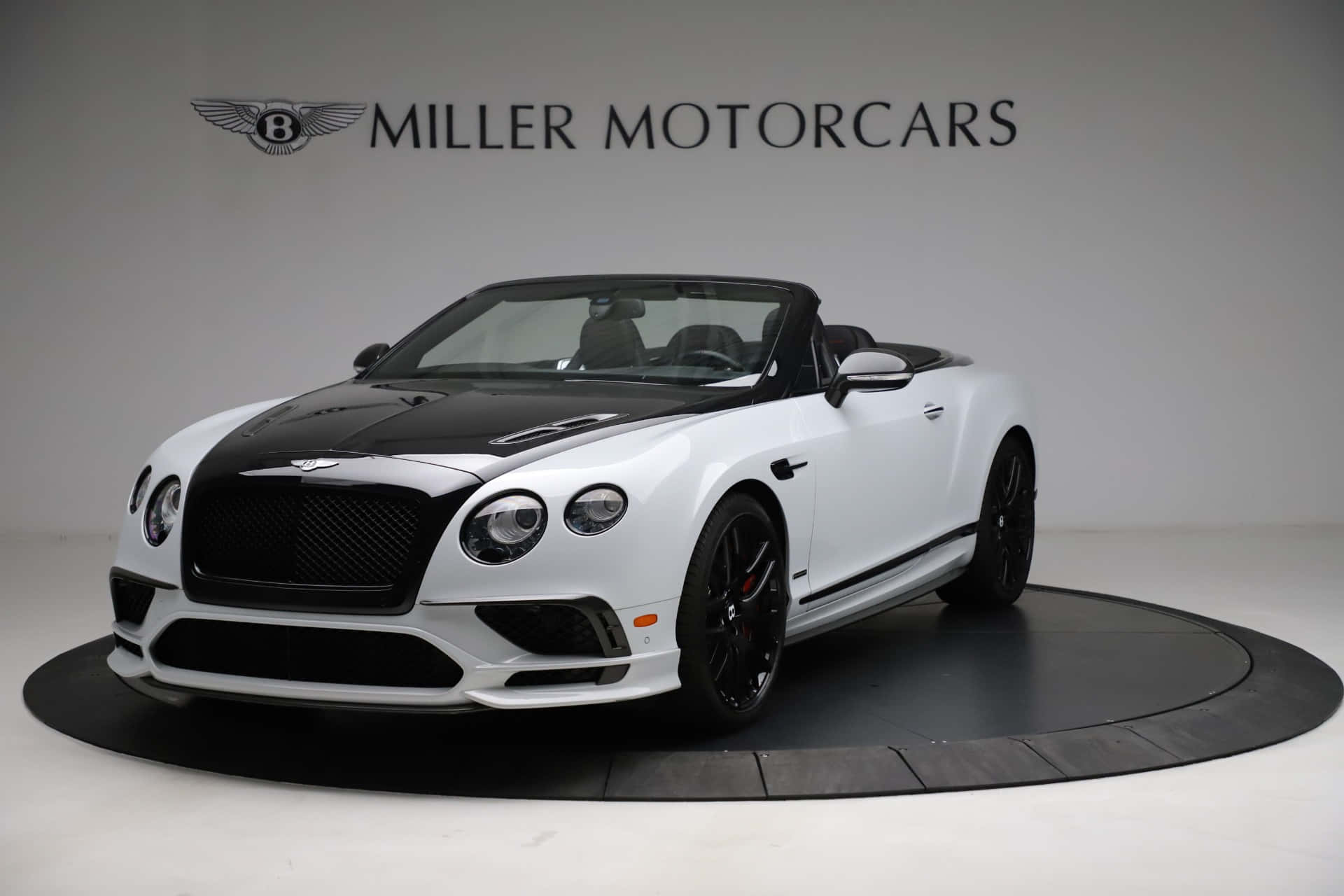 Bentley Continental Supersports 桌布 壁紙 — 一輛純白色的賓利 Continental GT 開篷車，帶有黑色飾邊和輪圈，在工作室燈光下展示於圓形平台上。