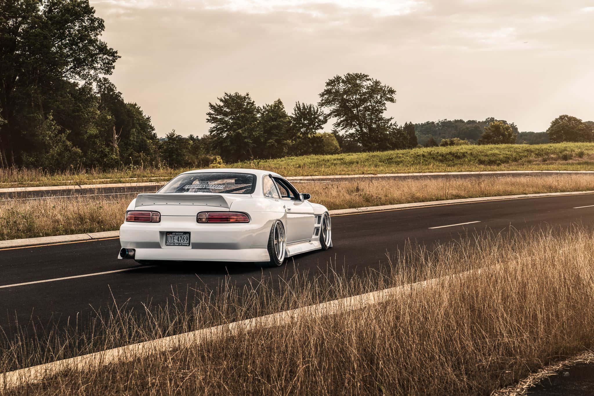 Lexus Sc 300 桌布 壁紙 — 一輛白色改裝跑車在鄉村高速公路上飄移，兩旁是金色的草地和樹木，天空是柔和的日落景色。
