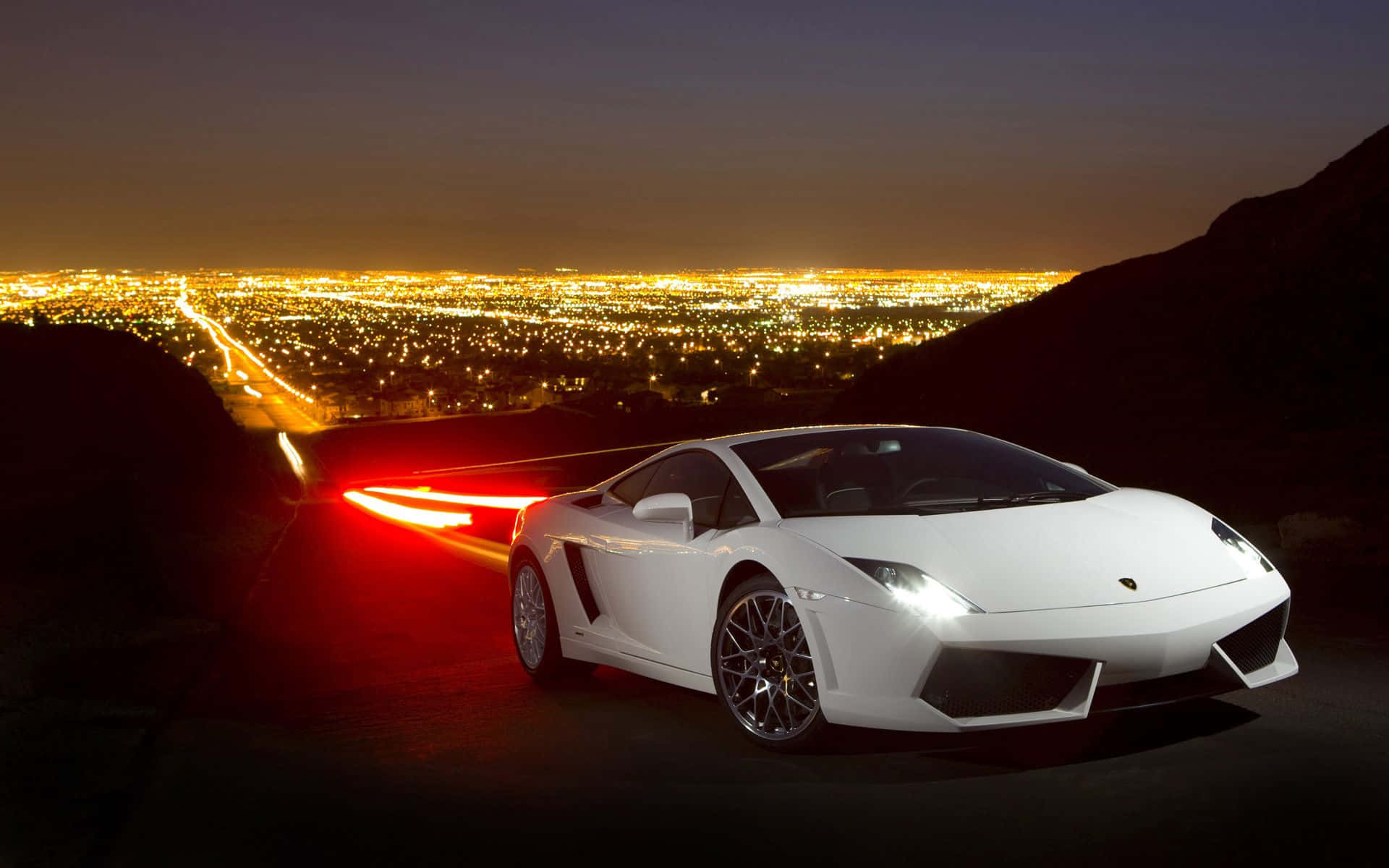 Lamborghini Gallardo 桌布 壁紙 — 一輛白色林寶堅尼跑車在夜間滑行，紅色尾燈閃爍，背景是廣闊的金色燈光城市景觀。