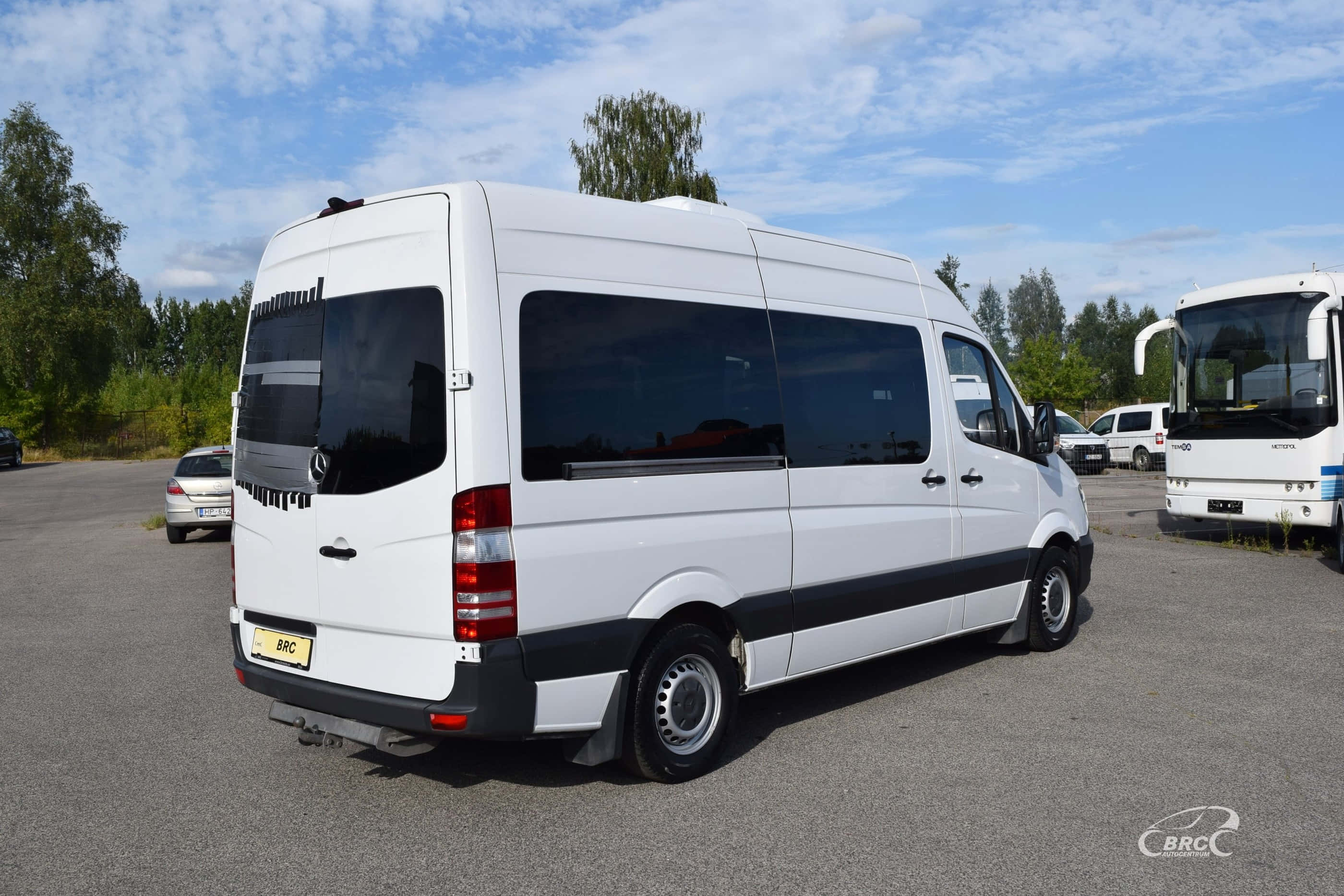 Mercedes Benz Sprinter 桌布 壁紙 — 一架白色 Mercedes-Benz Sprinter 客貨車停泊在停車場，天空局部多雲，附近有樹木及其他車輛。