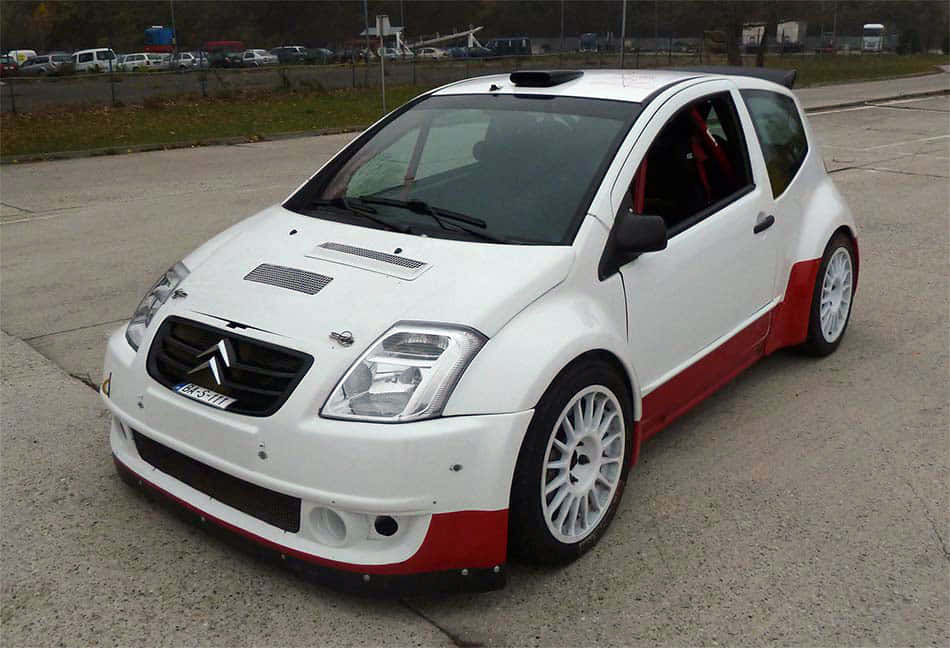 Citroen C2 Super 1600 桌布 壁紙 — 一架白色和紅色改裝嘅雪鐵龍C3拉力賽車停泊喺有草地背景嘅混凝土場地上。