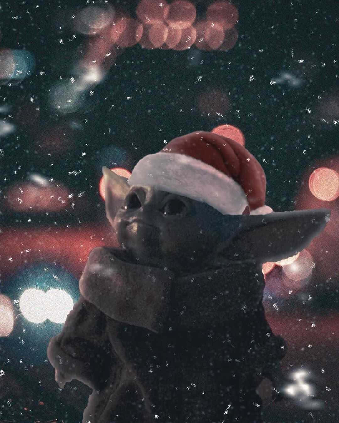 Baby Yoda 圣誕雪景 壁紙 — 一個戴住紅色聖誕帽嘅細小外星細路企喺落緊雪嘅地方，後面有模糊嘅城市燈光閃爍。