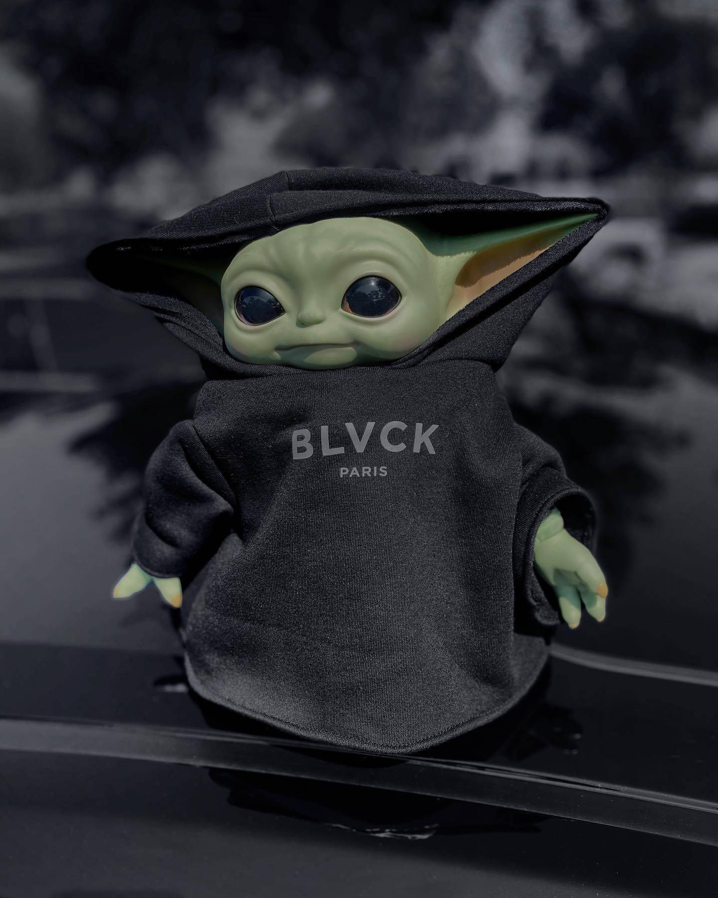 Baby Yoda毛公仔著黑色連帽衛衣，印有BLVCK PARIS字樣，坐喺車頭蓋上。