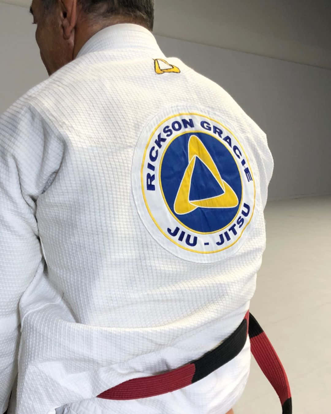  壁紙 — 一名男子身穿白色Rickson Gracie柔術道服，配紅黑腰帶，背對純白牆壁。