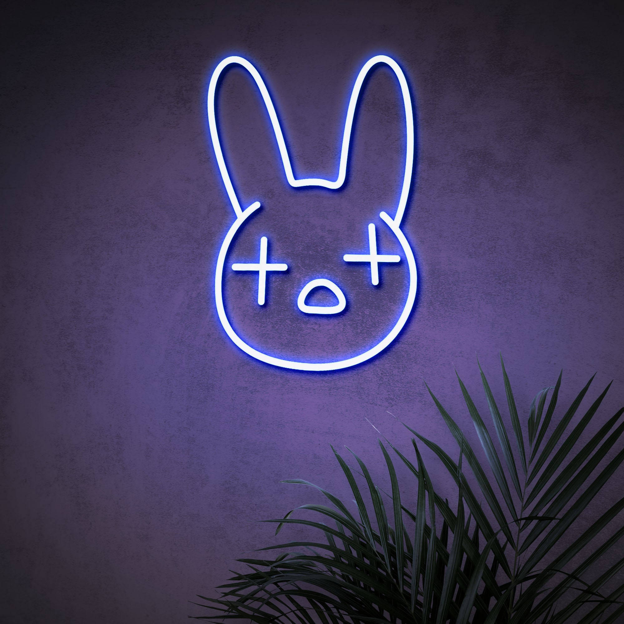 官方 Bad Bunny 標誌 壁紙 — 一個發光的藍色霓虹兔頭，帶有X形眼睛和O形嘴巴，安裝在紫色牆壁上，上方有綠色棕櫚葉。