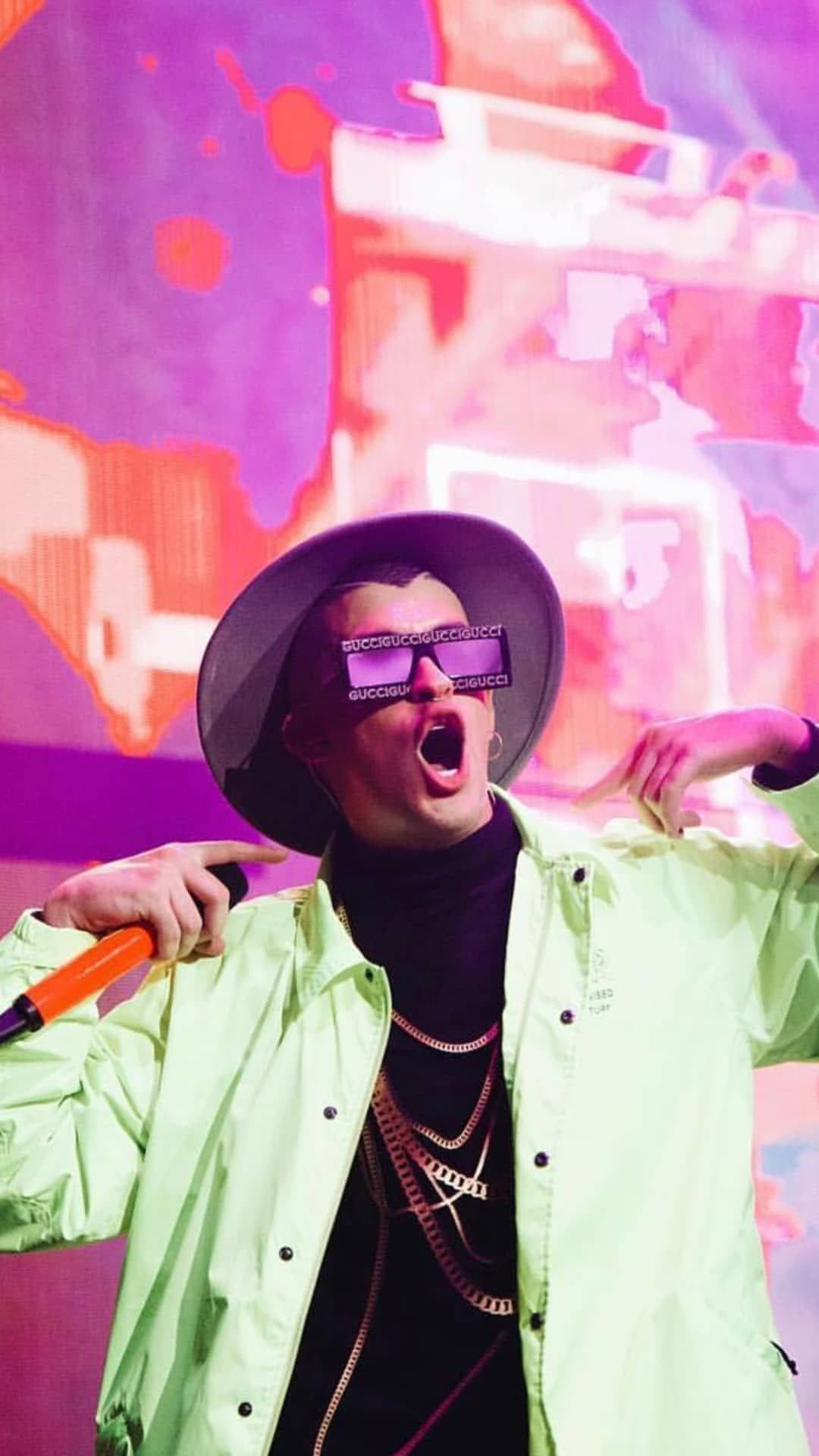 Bad Bunny 穿霓虹綠波羅衫 壁紙 — 一個人穿著霓虹外套和超大太陽眼鏡，對著充滿活力的粉紅色和紫色抽象背景激動地尖叫。