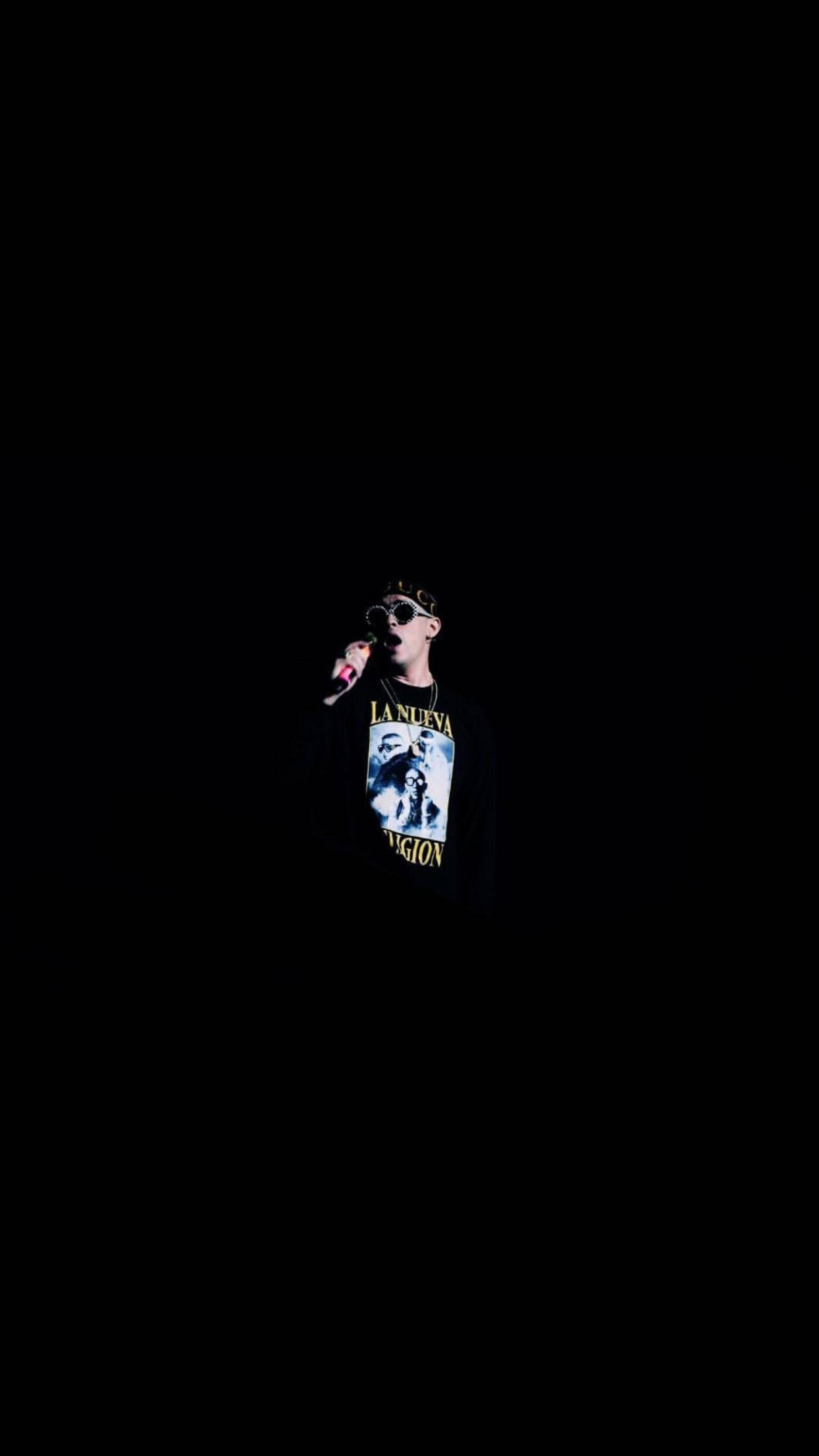 Bad Bunny 黑色極簡海報 壁紙 — 一個穿著深色T恤和太陽眼鏡的人，在純黑背景下拿著麥克風。