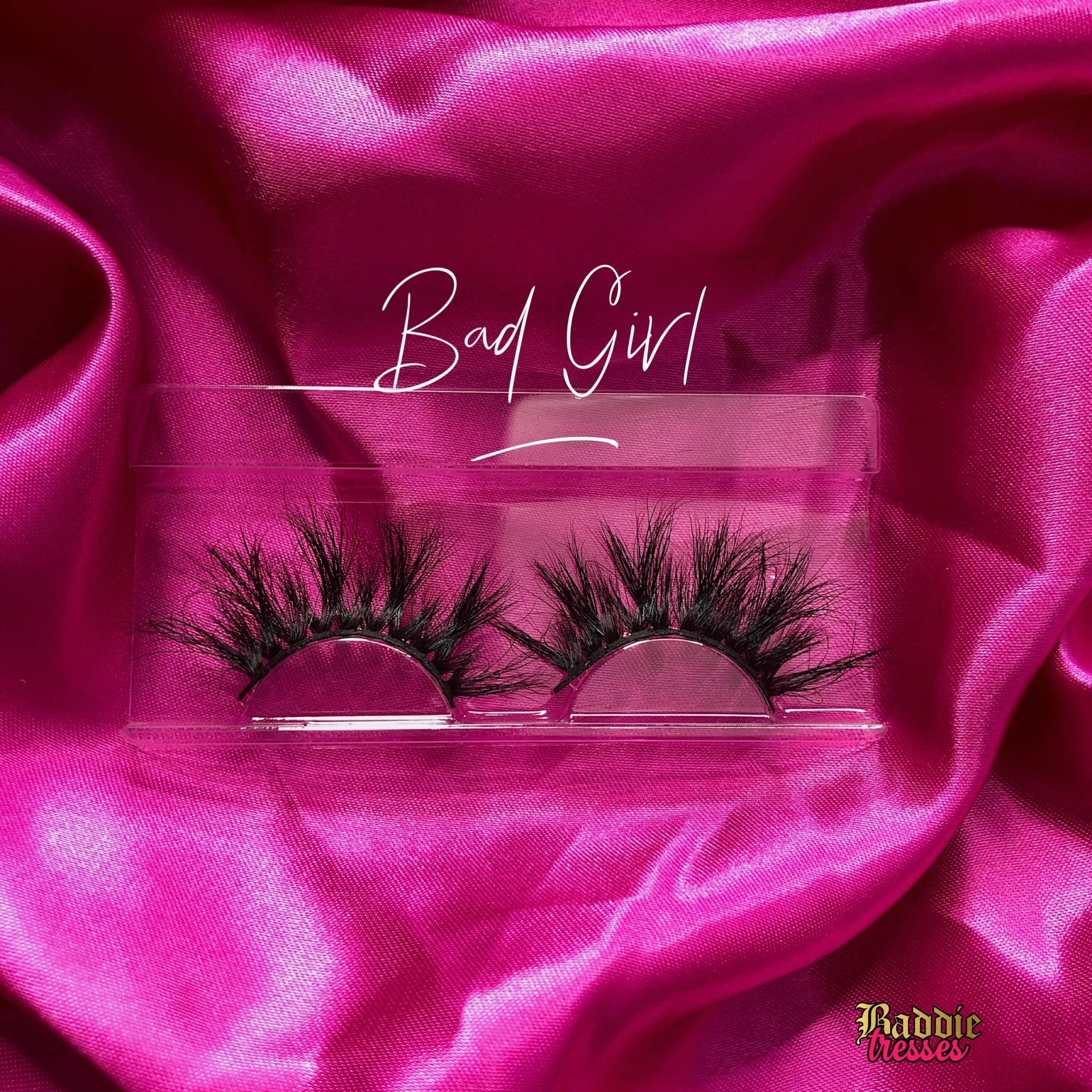 透明盒中的黑色假睫毛，放在粉紅色緞面上，帶有「Bad Girl」文字。