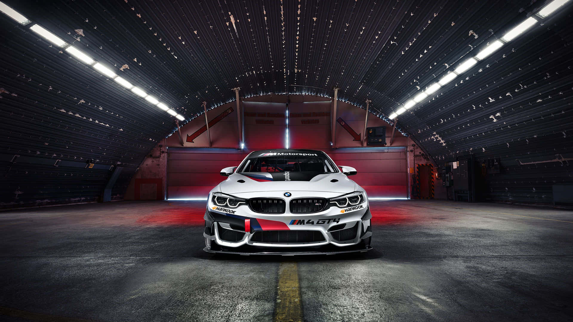 白色BMW M4 GT4賽車在黑暗的工業車庫中，帶有紅色燈光點綴。