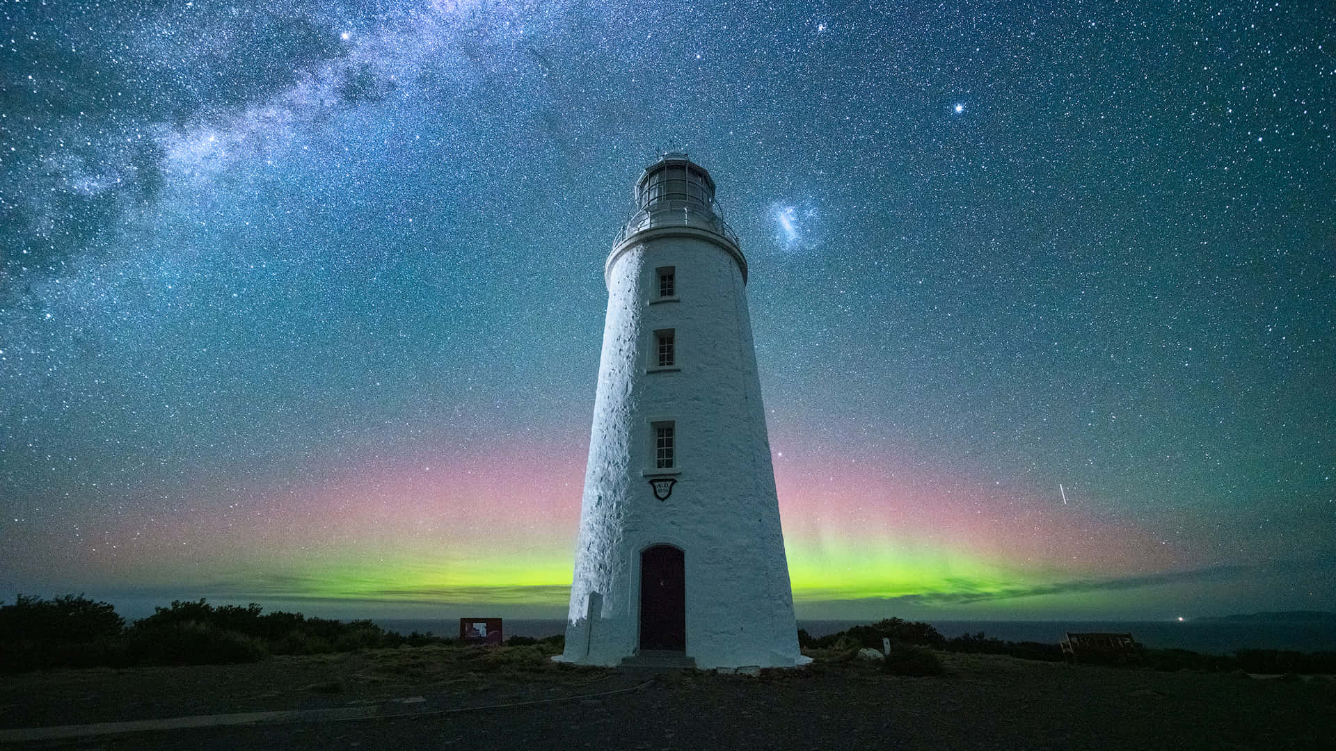  壁紙 — 一座白色燈塔在星空下高聳，銀河和充滿活力的綠色北極光在上方閃耀。