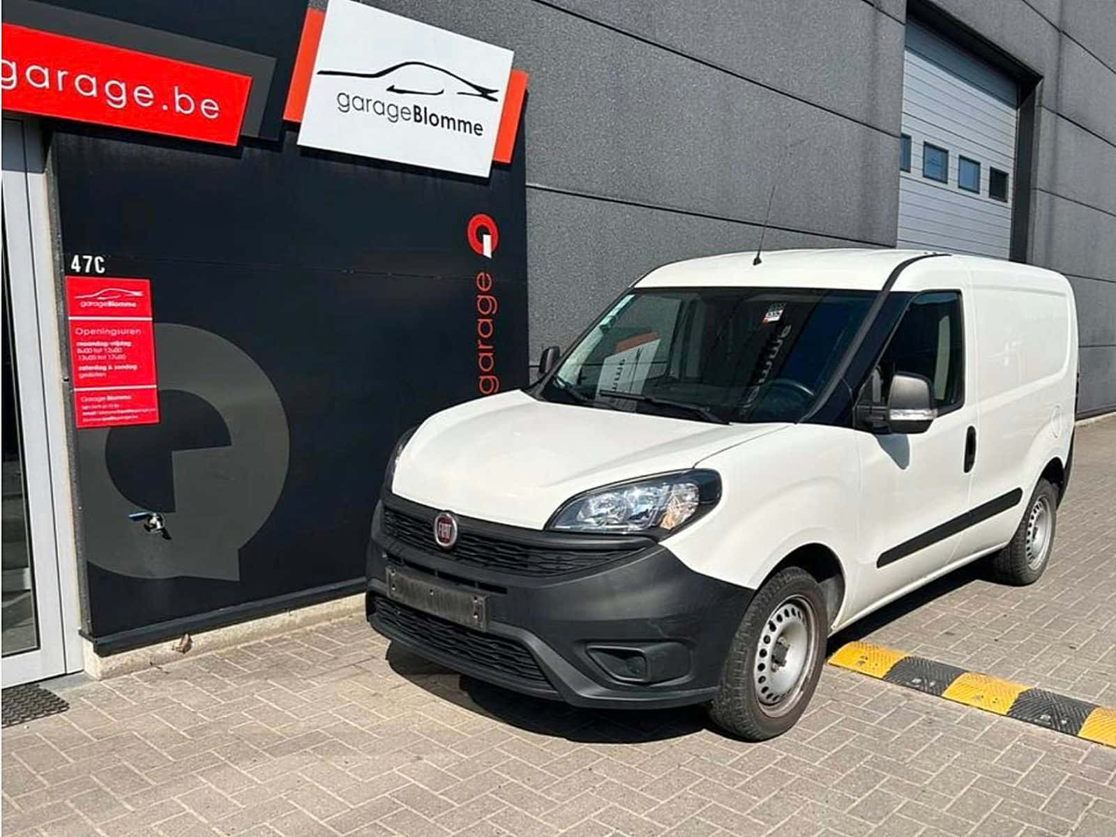  壁紙 — 一輛白色Fiat Fiorino客貨車停泊在現代化車庫外的鋪砌場地上，車庫帶有醒目的招牌。