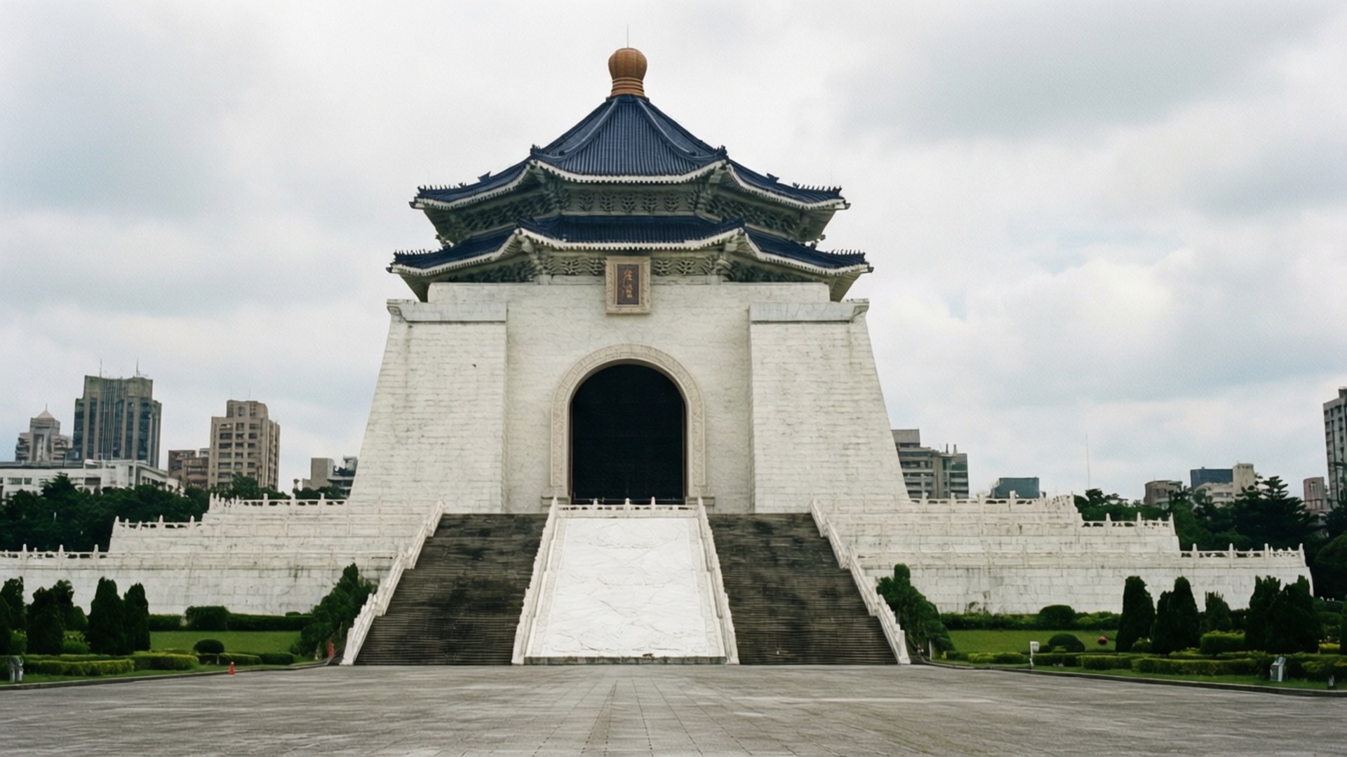 Taiwan 桌布 壁紙 — 白色宏偉的中正紀念堂，藍色琉璃瓦屋頂，在陰天之下，聳立於修剪整齊的花園和城市天際線之間。