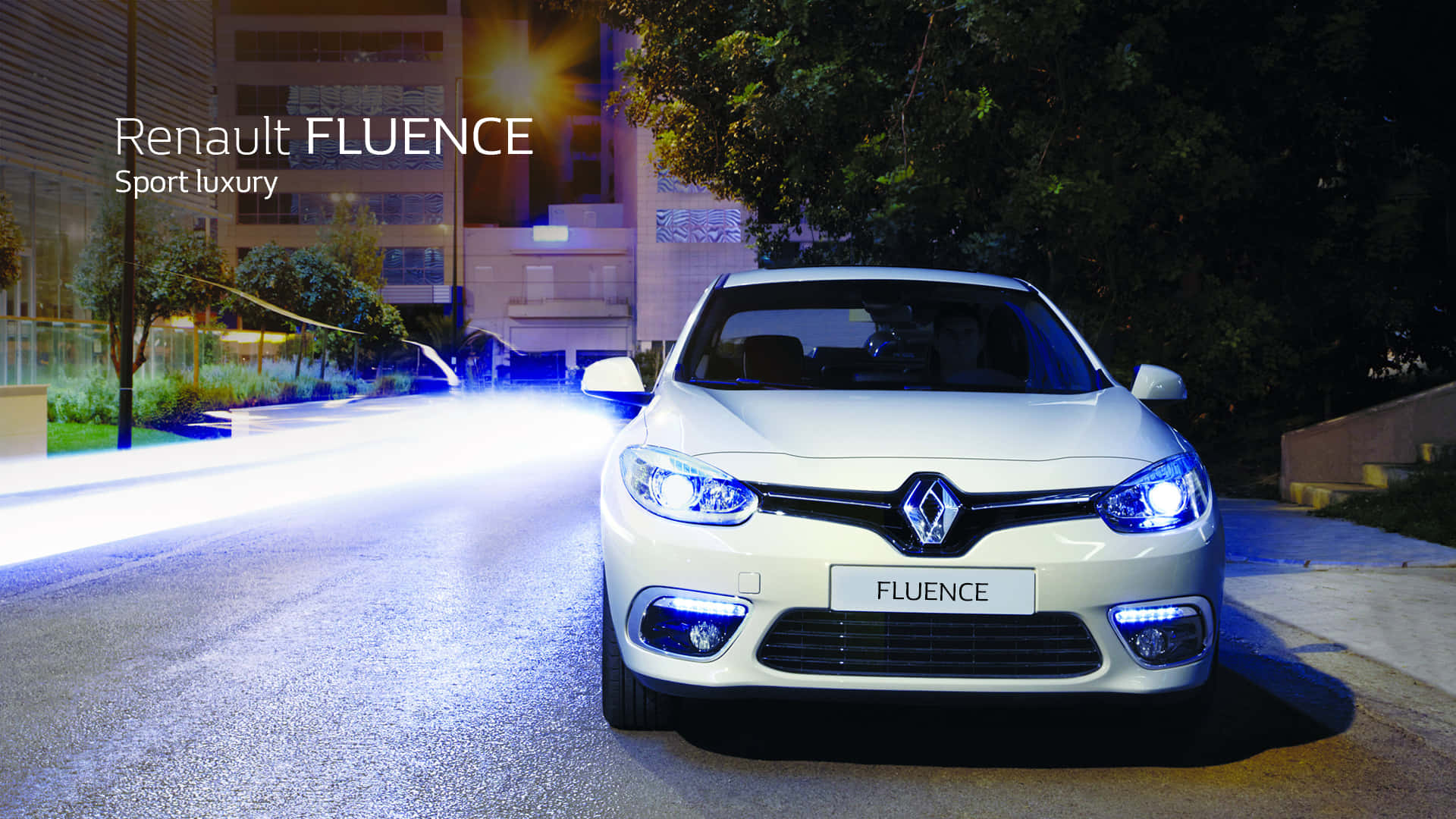 Renault Fluence 桌布 壁紙 — 一輛白色雷諾Fluence在夜間向前滑行，閃亮的車頭燈照亮了一條濕漉漉的、兩旁種滿樹木和建築物的城市街道。