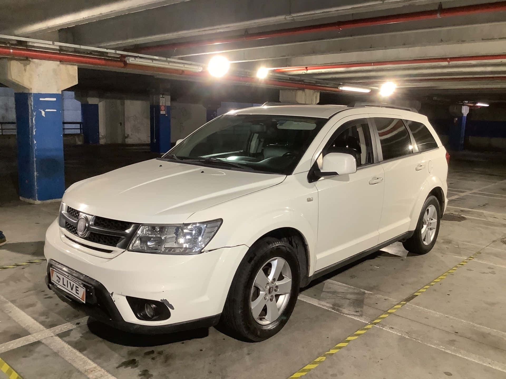  壁紙 — 一輛白色旅行車停泊在光線昏暗的地下停車場，地面有黃色條紋線，頭頂有暴露的管道。