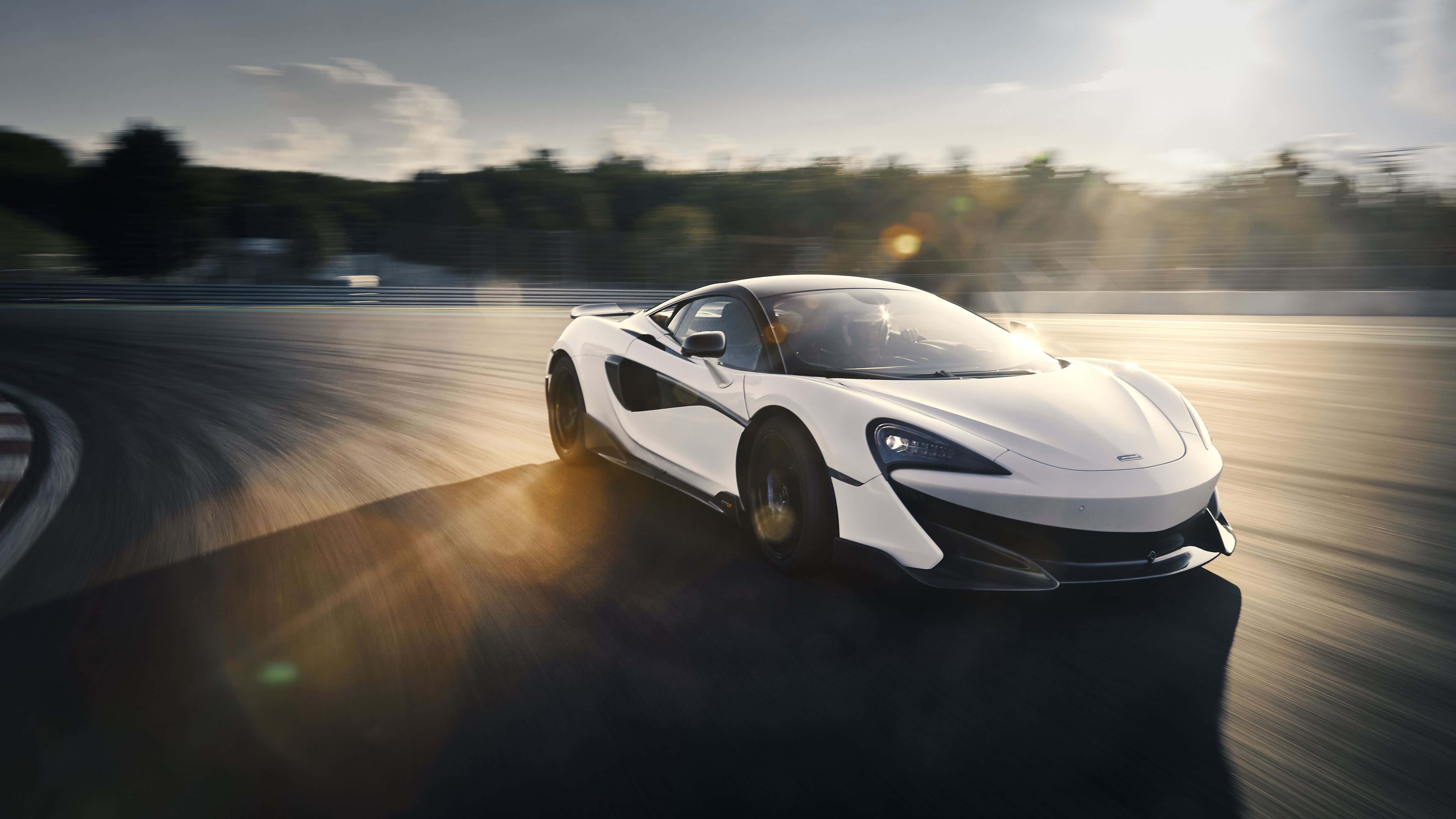 Mclaren 600lt 桌布 壁紙 — 一輛白色McLaren跑車在日落時分於賽道上疾馳，帶有動態模糊和金色鏡頭光暈。