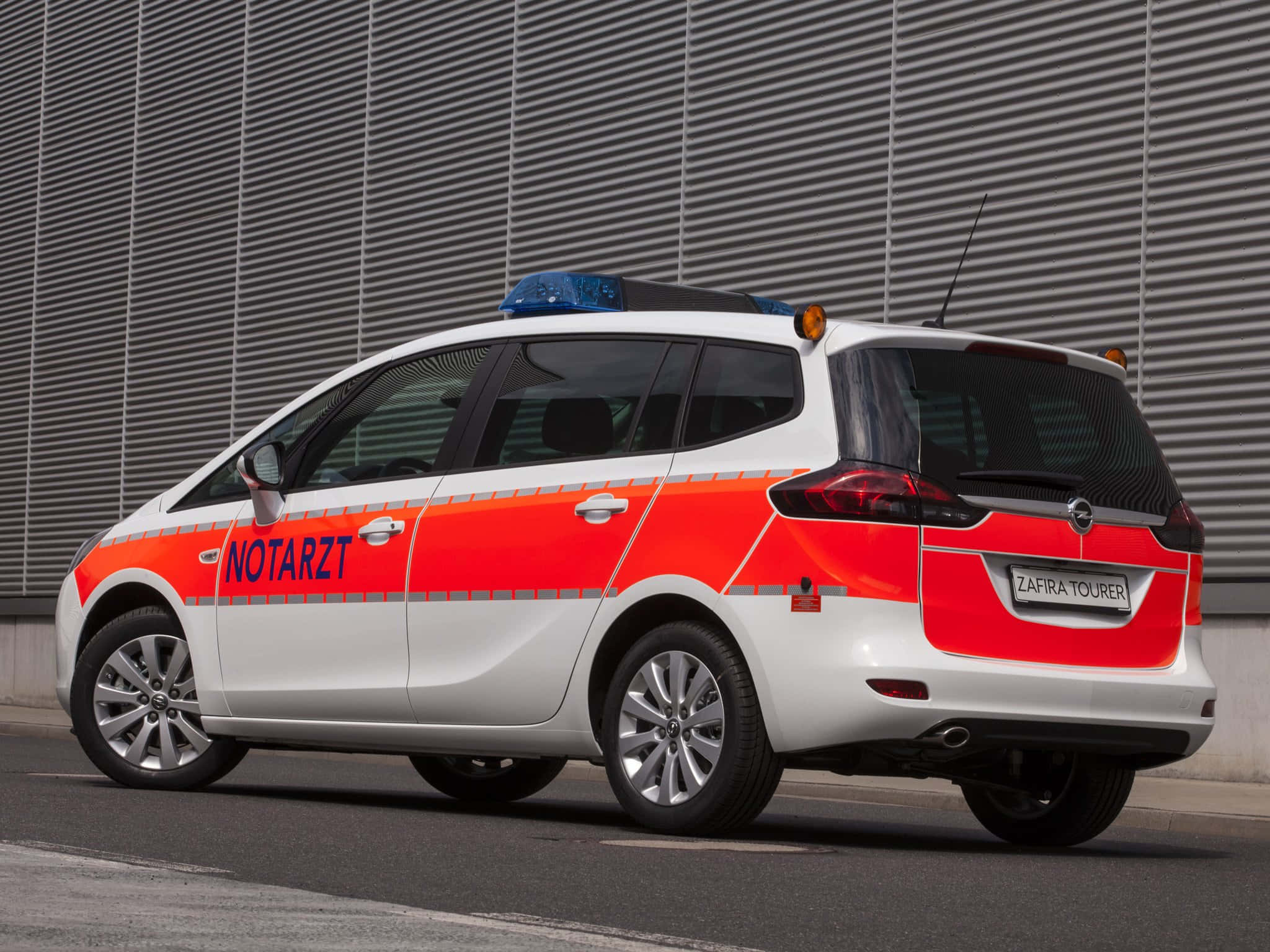 Opel Zafira 桌布 壁紙 — 一輛白色和橙色的德國緊急醫療服務車停泊在灰色波紋金屬牆旁。