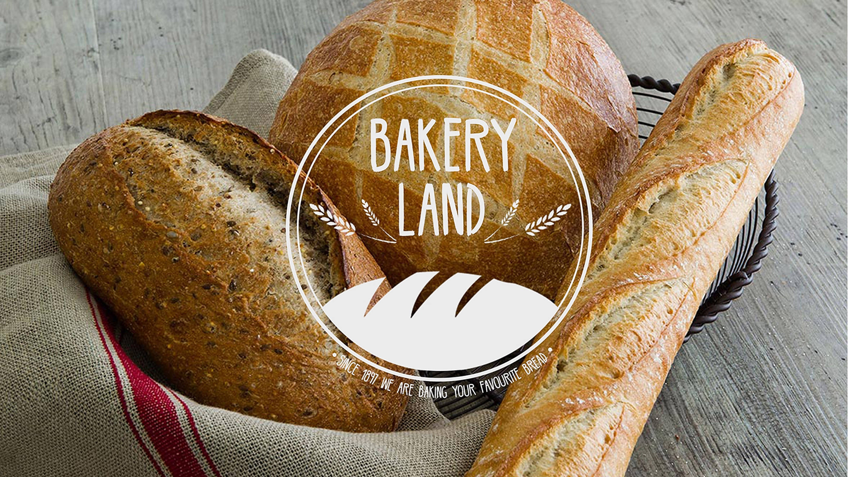 Bakery Land 面包 壁紙 — 新鮮出爐的工匠麵包，包括一個圓形麵包和法式長棍麵包，放在一個鋪有紅白條紋布的鐵絲籃子裡，置於木質表面上。