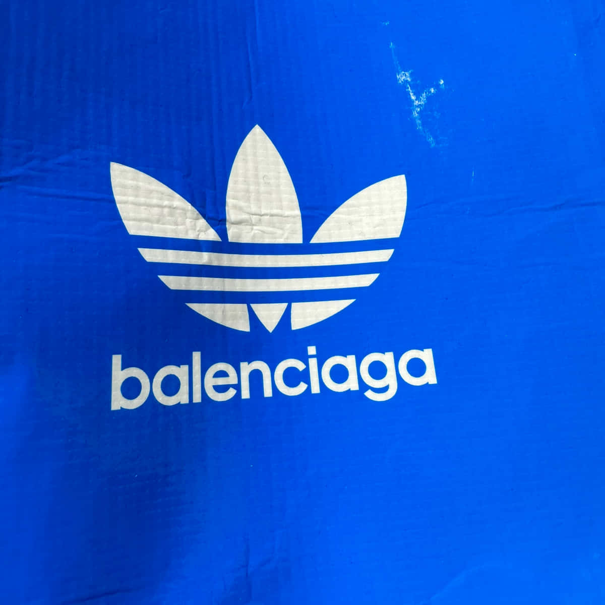 以Balenciaga奢華時尚漫步街頭 壁紙 — 近距離拍攝的鮮豔藍色布料，上面印有白色Adidas三葉草標誌和Balenciaga文字。